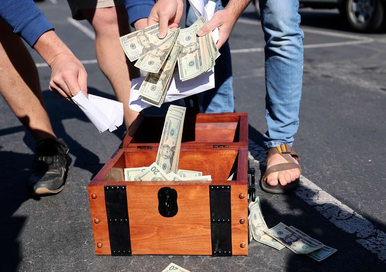 John Maxim, left, and David Cline put $20,000 into a chest during a press conference in the Best Buy parking lot in South Salt Lake on Tuesday, May 31, 2022, as they announce plans to hide the money in the Utah wilderness. This is the fourth time they’ve organized a treasure hunt. Maxim and Cline said it will be very close to a hiking trail and won’t require any digging. The chest pictured was made for them by a fan of the treasure hunts but will not be used to hide the treasure.