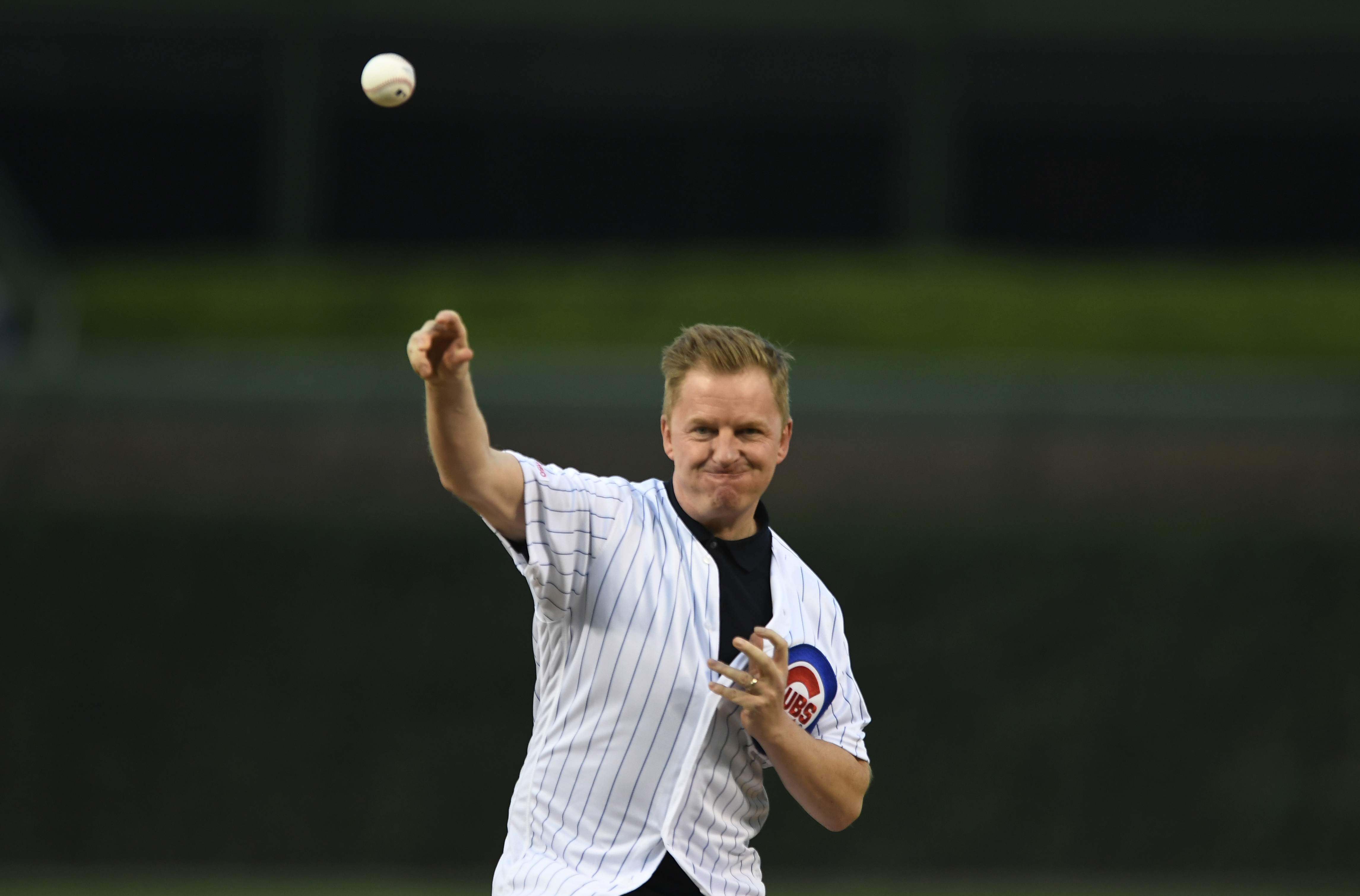 FILE - NBC Sports Premier League play-by-play broadcast announcer Arlo White throws out a ceremonial first pitch before a baseball game between the Chicago Cubs and the Seattle Mariners on Sept. 3, 2019, at Wrigley Field in Chicago. White will not return to NBC’s coverage of the Premier League when the season begins in August, a person with knowledge of the situation told The Associated Press. White will be replaced by Peter Drury, who has been calling the top Premier League games since 1998, recently on the league’s world feed.