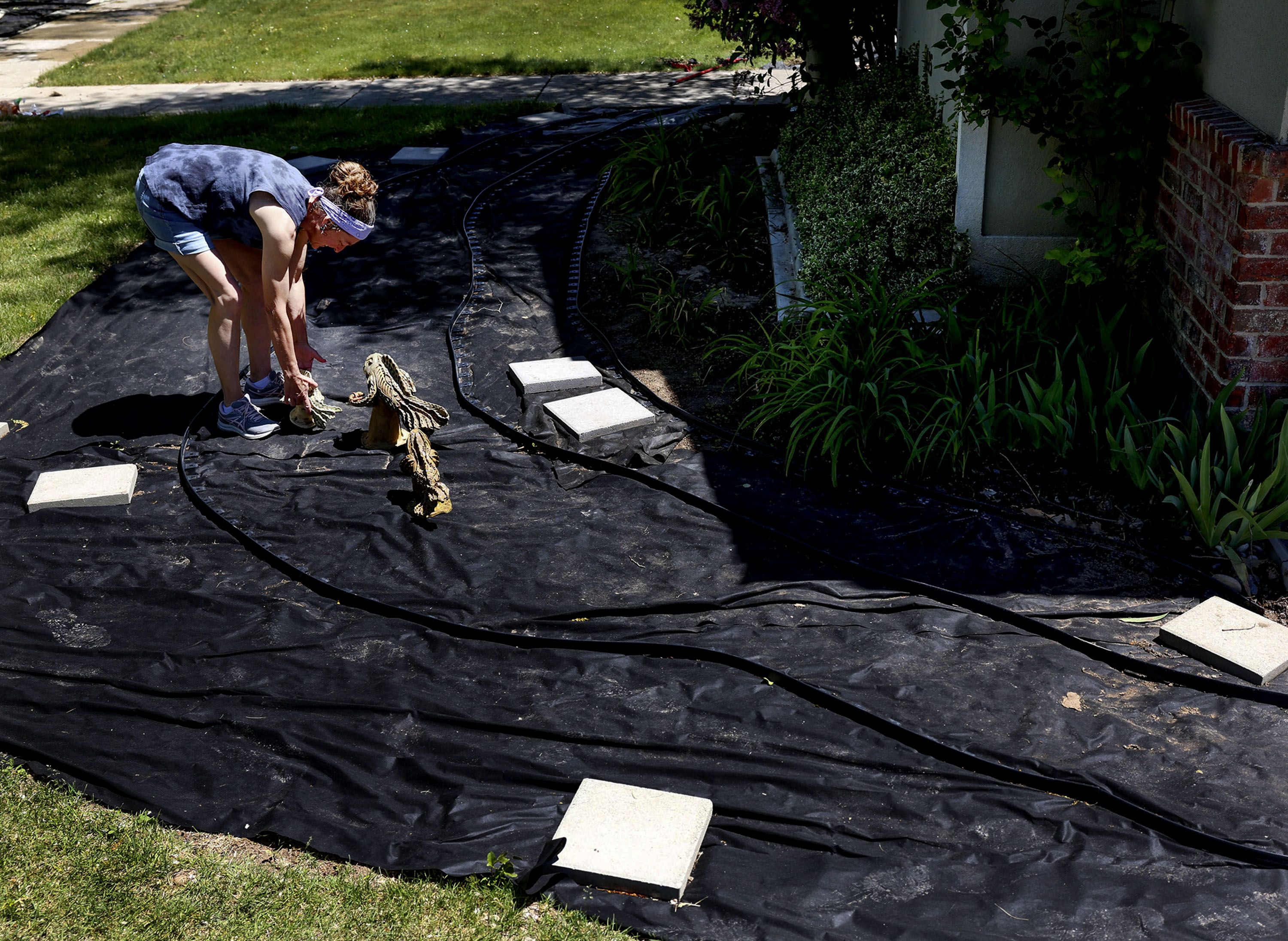 Shalise Marx arranges ceramic fish while working on a xeriscaping project in her yard in Layton on Thursday. The fish will be swimming in a river of colored rocks once the project is completed.