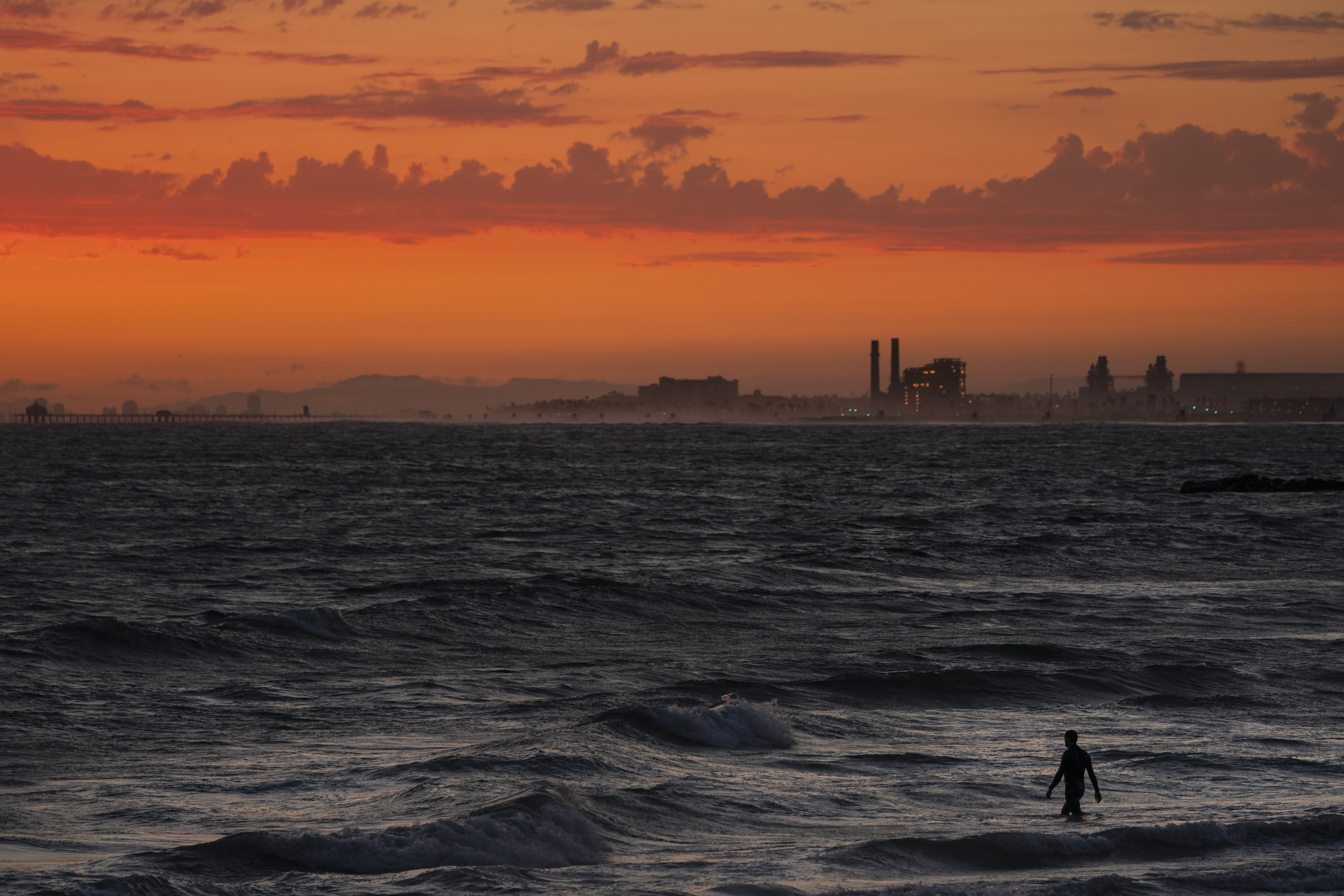 A man wades into the ocean at sunset on June 22, 2021, in Newport Beach, Calif. The National Oceanic and Atmospheric Administration announced Friday that levels of the main global warming gas have shot past a key milestone, more than 50% higher than pre-industrial levels.