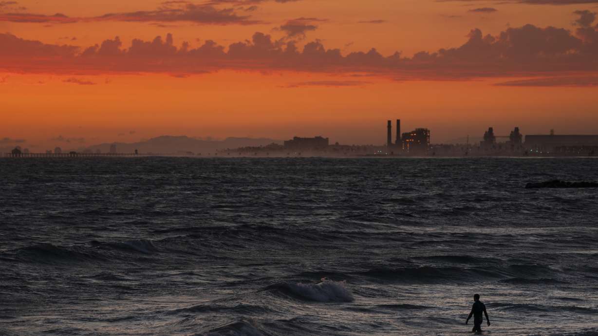 A man wades into the ocean at sunset on June 22, 2021, in Newport Beach, Calif. The National Oceanic and Atmospheric Administration announced Friday that levels of the main global warming gas have shot past a key milestone, more than 50% higher than pre-industrial levels.