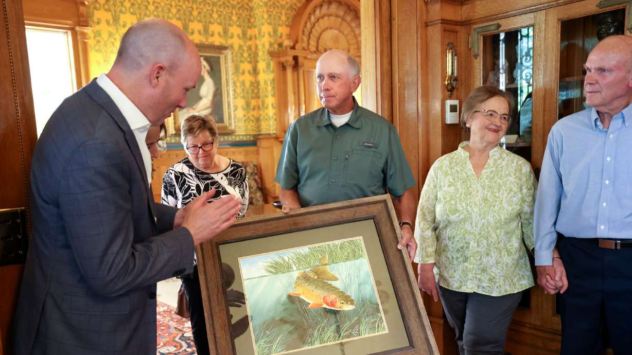 Gov. Spencer Cox, left, accepts a painting of a Bonneville cutthroat trout from artist Paul Twitchell, third from left, before a dinner for the longest lifetime state fishing license holders at the Governor’s Mansion in Salt Lake City on May 25, as Caroline Twitchell, second from left, Carol Smith and Cecil Smith look on.