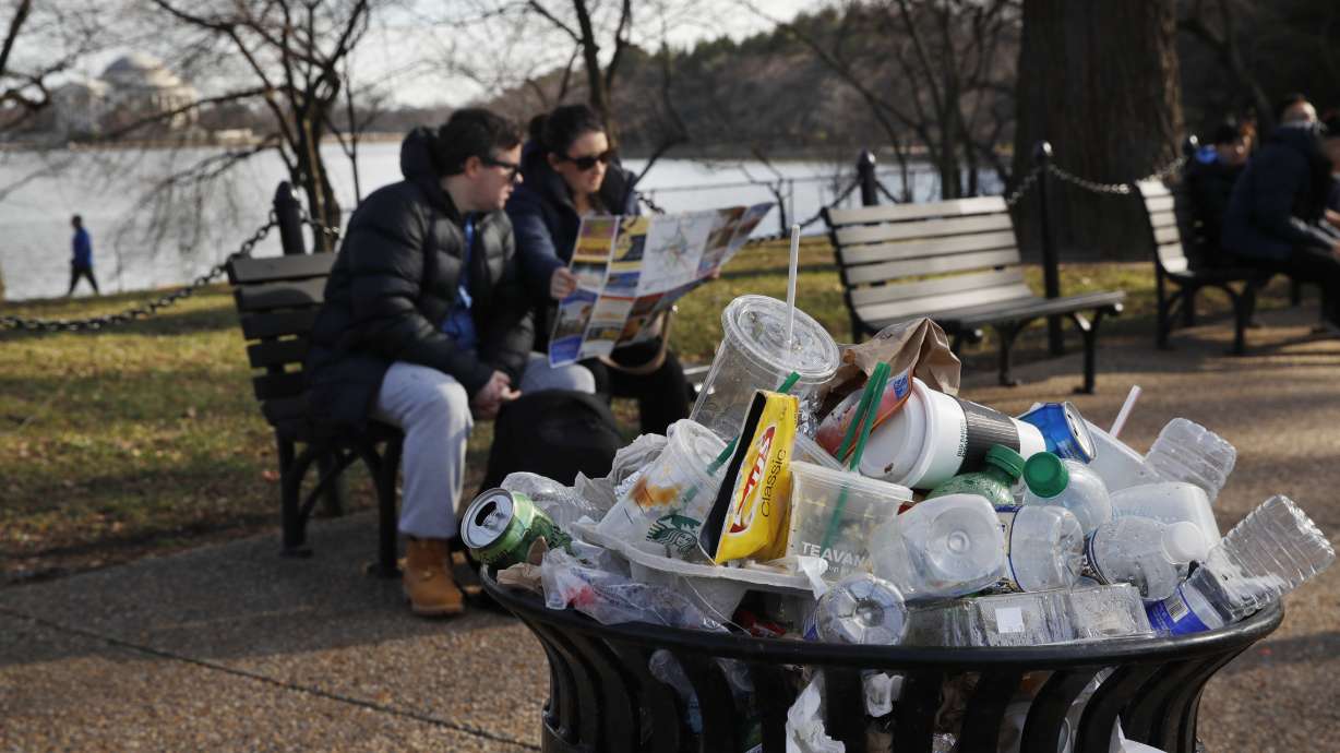 A trash can overflows as people sit outside of the Martin Luther King Jr. Memorial by the Tidal Basin, Dec. 27, 2018, in Washington, during a partial government shutdown. The Interior Department said Wednesday it will phase out single-use plastic products on national parks and other public lands over the next decade.