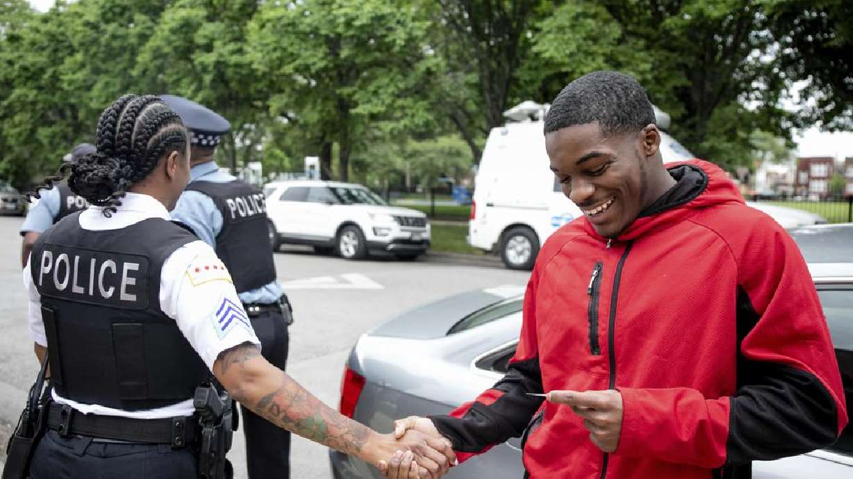 A police officer shakes hands with Anthony Perry, 20, after Early Walker, founder of the organization I'm Telling Don't Shoot, surprised Perry with a free car, Wednesday morning in Chicago. Walker surprised Perry with the car after video of him saving a man from being shocked after falling onto the 59th Street red line train tracks went viral earlier in the week.