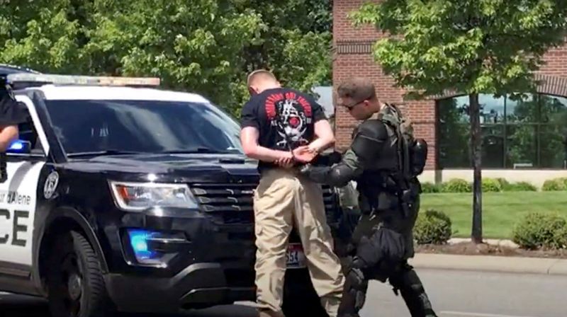 A man is detained by a police officer in riot gear, as the police guard a group of men, who police say are among 31 arrested for conspiracy to riot and are affiliated with the group Patriot Front, after they were found in the rear of a U-Haul van in the vicinity of a Pride event in Coeur d'Alene, Idaho, Saturday.