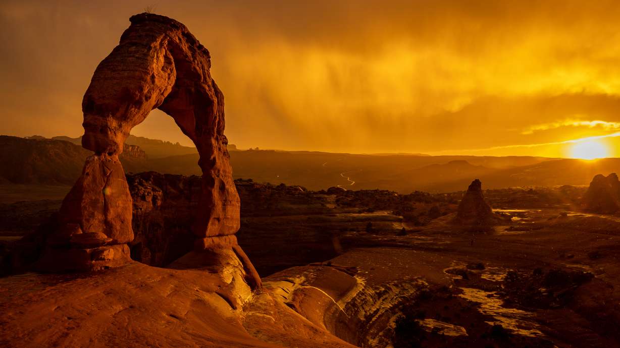 The sun sets as a rainstorm blows over Delicate Arch in Arches National Park near Moab on Sept. 18, 2021. A new shuttle service between Moab and the park debuted on Tuesday as part of a pilot program.