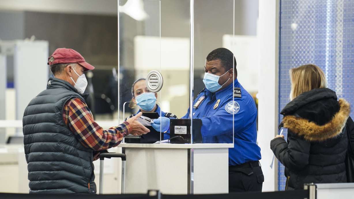 A Transportation Security Administration agent serves a traveler at a checkpoint in a sparsely populated Terminal B at LaGuardia Airport, Nov. 25, 2020, in the Queens borough of New York. Airlines are canceling more than 1,400 flights across the U.S., Thursday, in one of the worst days yet in the summer travel season.