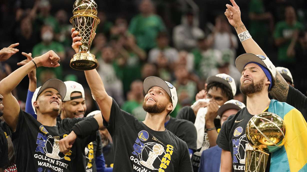 Golden State Warriors guard Stephen Curry, center, holds up the Bill Russell Trophy for most valuable player after the Warriors defeated the Boston Celtics in Game 6 to win basketball's NBA Finals championship, Thursday, June 16, 2022, in Boston.