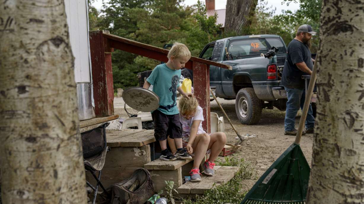 Harlee Holmes, 8, right, helps her brother Creek, 3, put his shoes on as the family packs up to leave their home that was damaged by severe flooding in Fromberg, Mont., Friday.