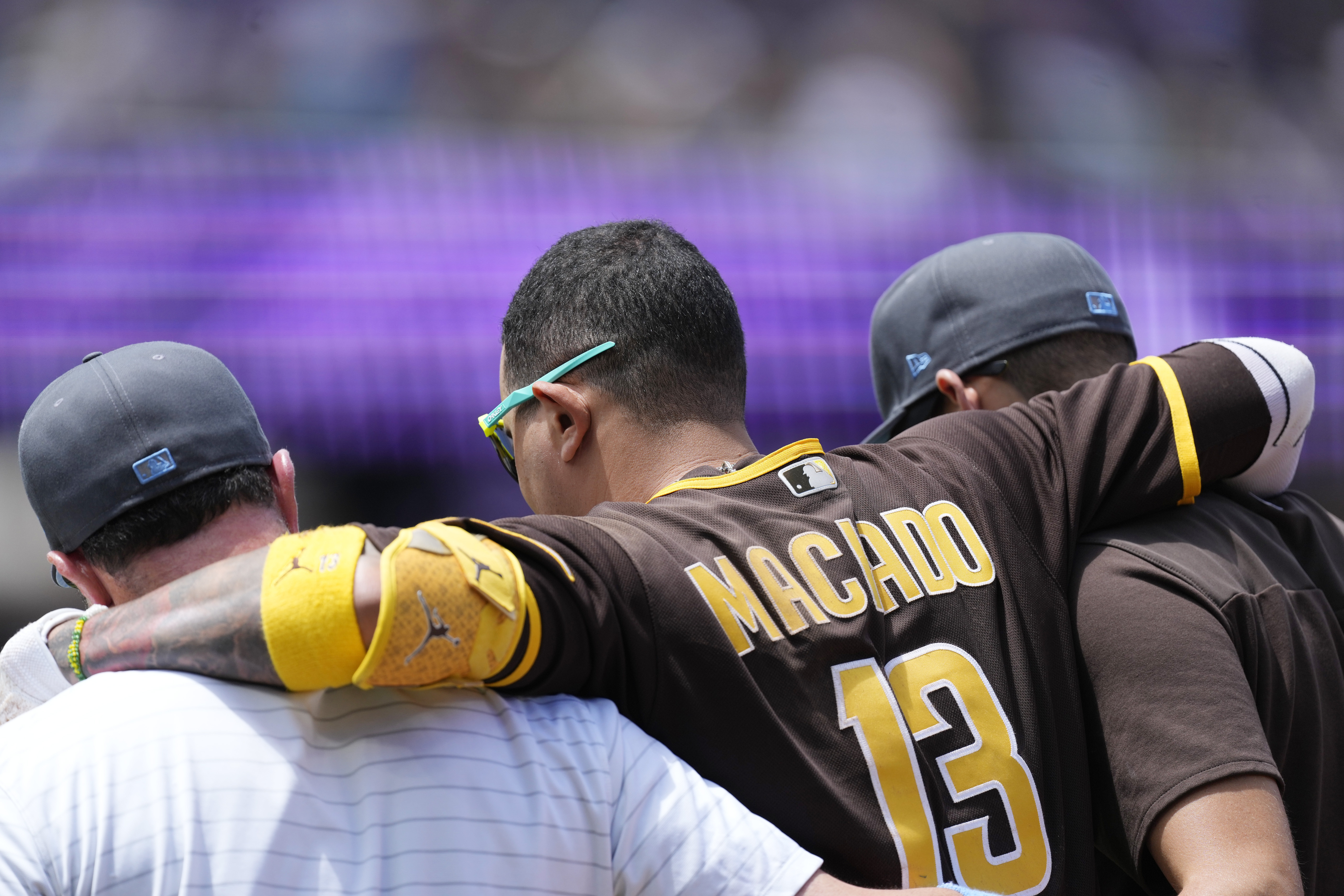 San Diego Padres' Manny Machado, center, is helped off the field after injuring his ankle while running out a ground ball hit to Colorado Rockies starting pitcher Antonio Senzatela in the first inning of a baseball game Sunday, June 19, 2022, in Denver. Machado was called out on the play. 