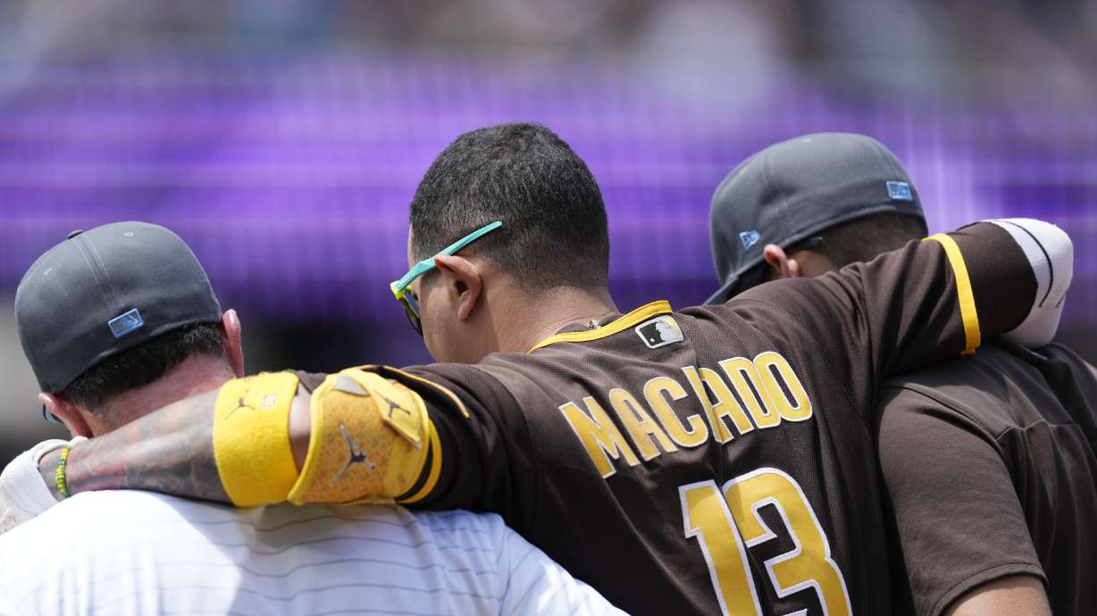 San Diego Padres' Manny Machado, center, is helped off the field after injuring his ankle while running out a ground ball hit to Colorado Rockies starting pitcher Antonio Senzatela in the first inning of a baseball game Sunday, June 19, 2022, in Denver. Machado was called out on the play.