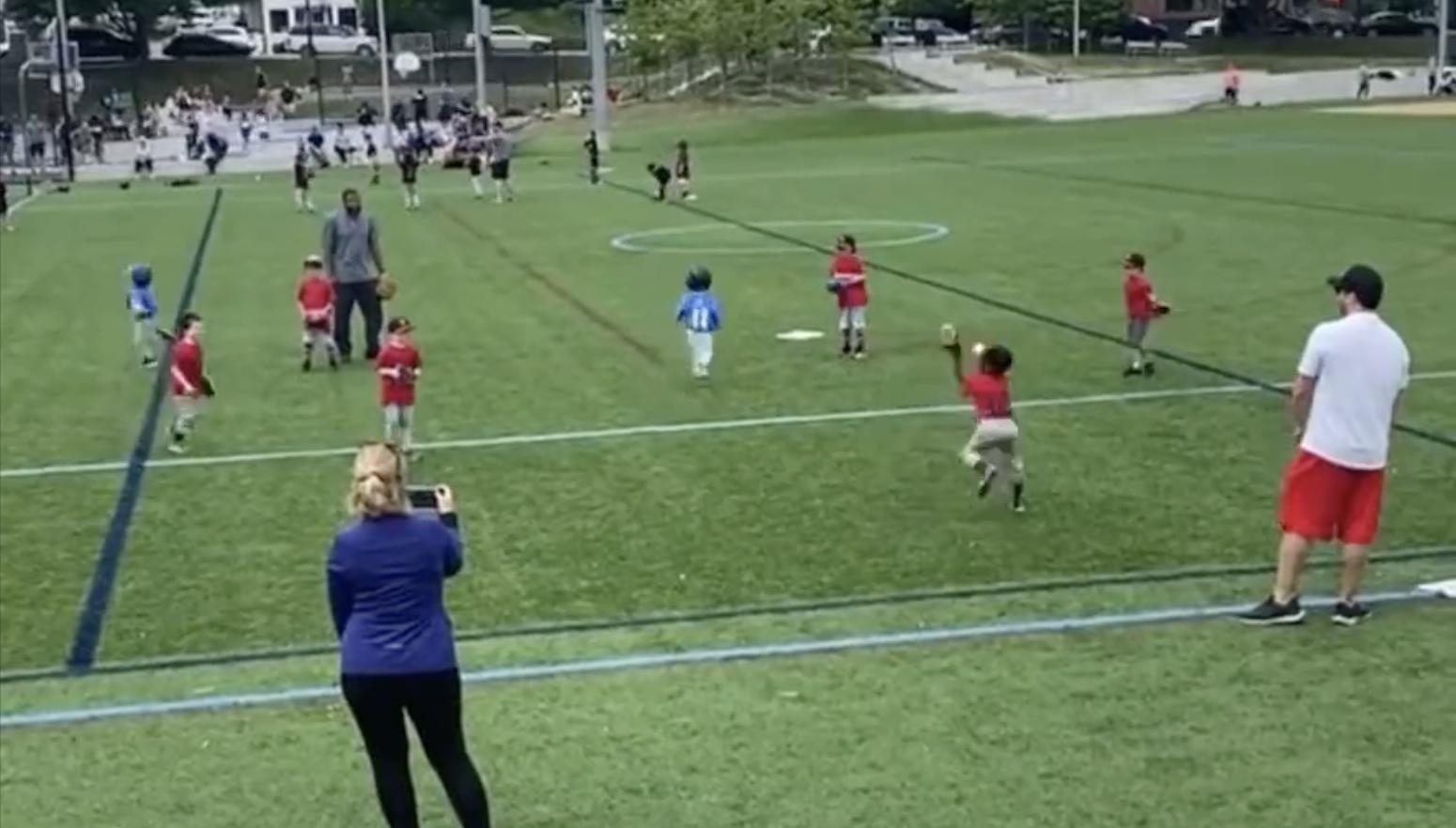A child is hit in the face by the ball during a tee-ball game as the batter skips first base and runs straight to second.