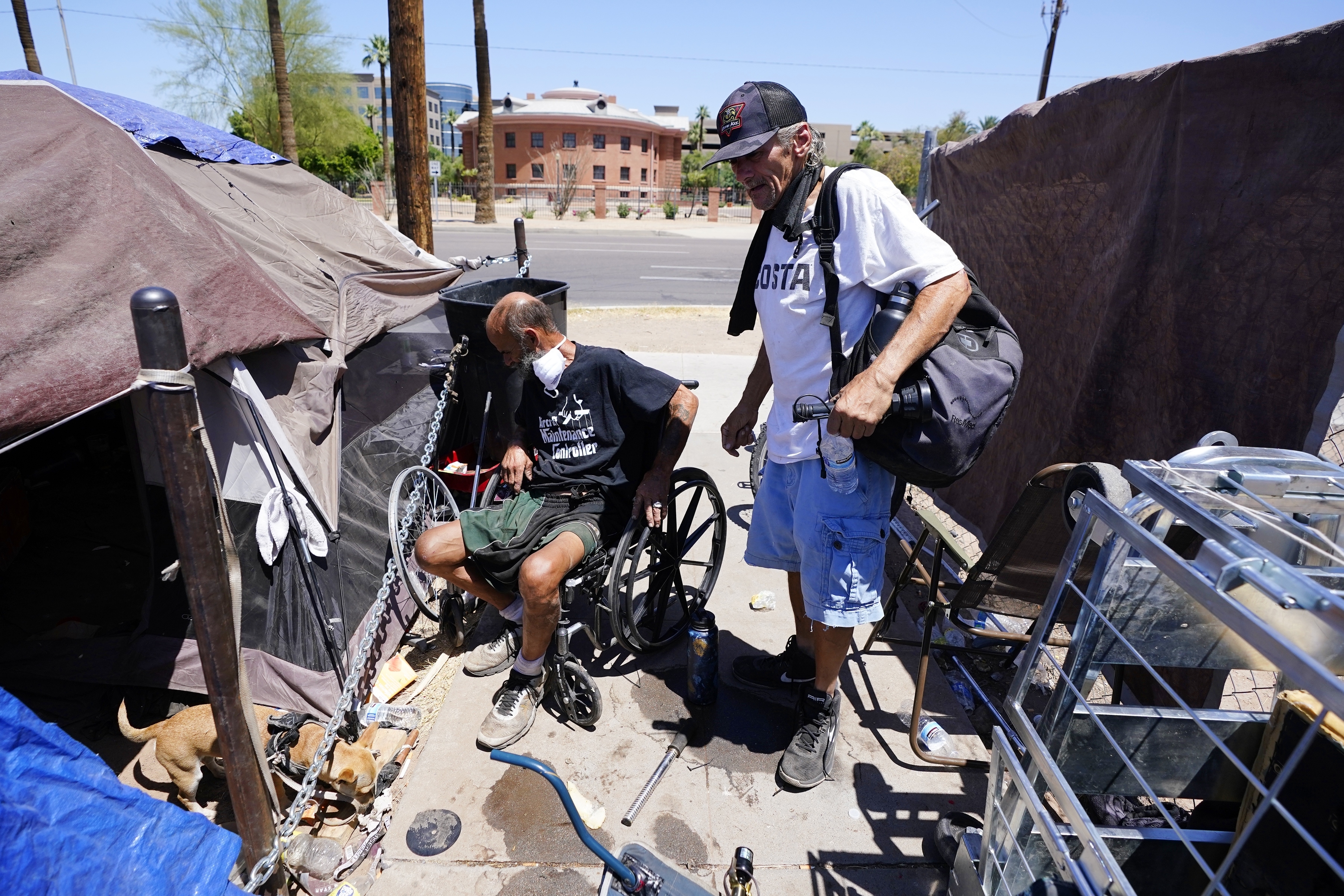 "Cueball", left, talks about his dog Lindsay with neighbor Terry Reed, right, at their tents May 20, in Phoenix. Hundreds of homeless people die in the streets each year from the heat, in cities around the U.S. and the world. The ranks of homeless have swelled after the pandemic and temperatures fueled by climate change soar. 