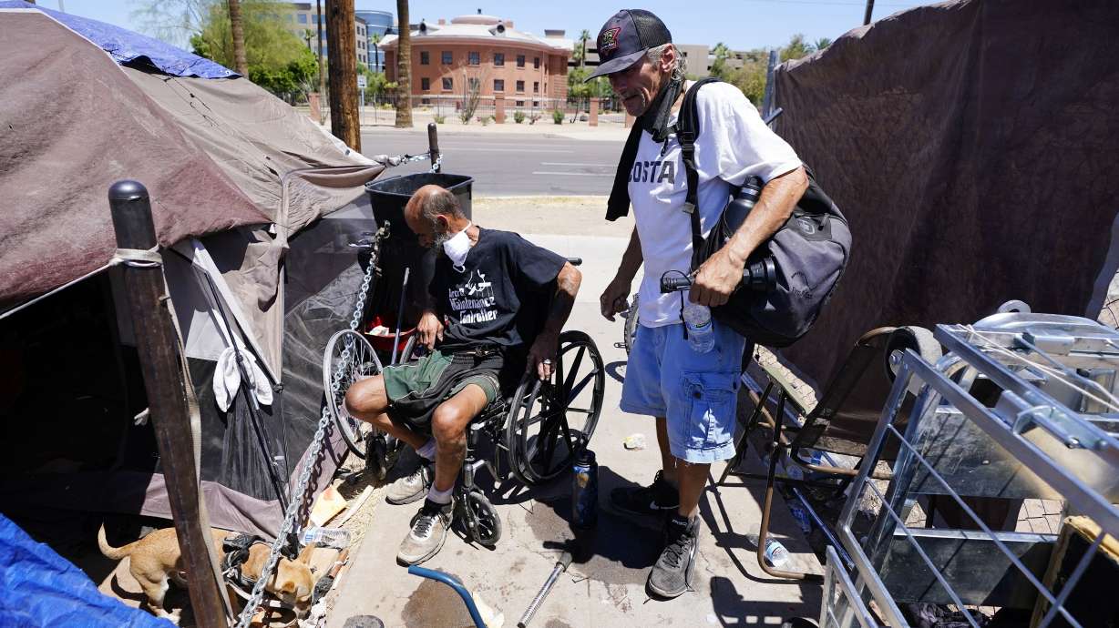 "Cueball", left, talks about his dog Lindsay with neighbor Terry Reed, right, at their tents May 20, in Phoenix. Hundreds of homeless people die in the streets each year from the heat, in cities around the U.S. and the world. The ranks of homeless have swelled after the pandemic and temperatures fueled by climate change soar.