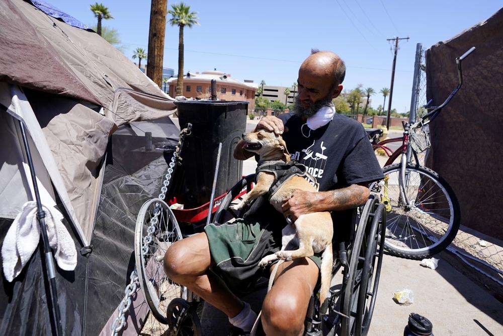 "Cueball" pets his dog Lindsay at their tent on the edge of a homeless encampment on May 20 in Phoenix. Hundreds of homeless people die in the streets each year from the heat, in cities around the U.S. and the world. The ranks of homeless have swelled after the pandemic and temperatures fueled by climate change soar.
