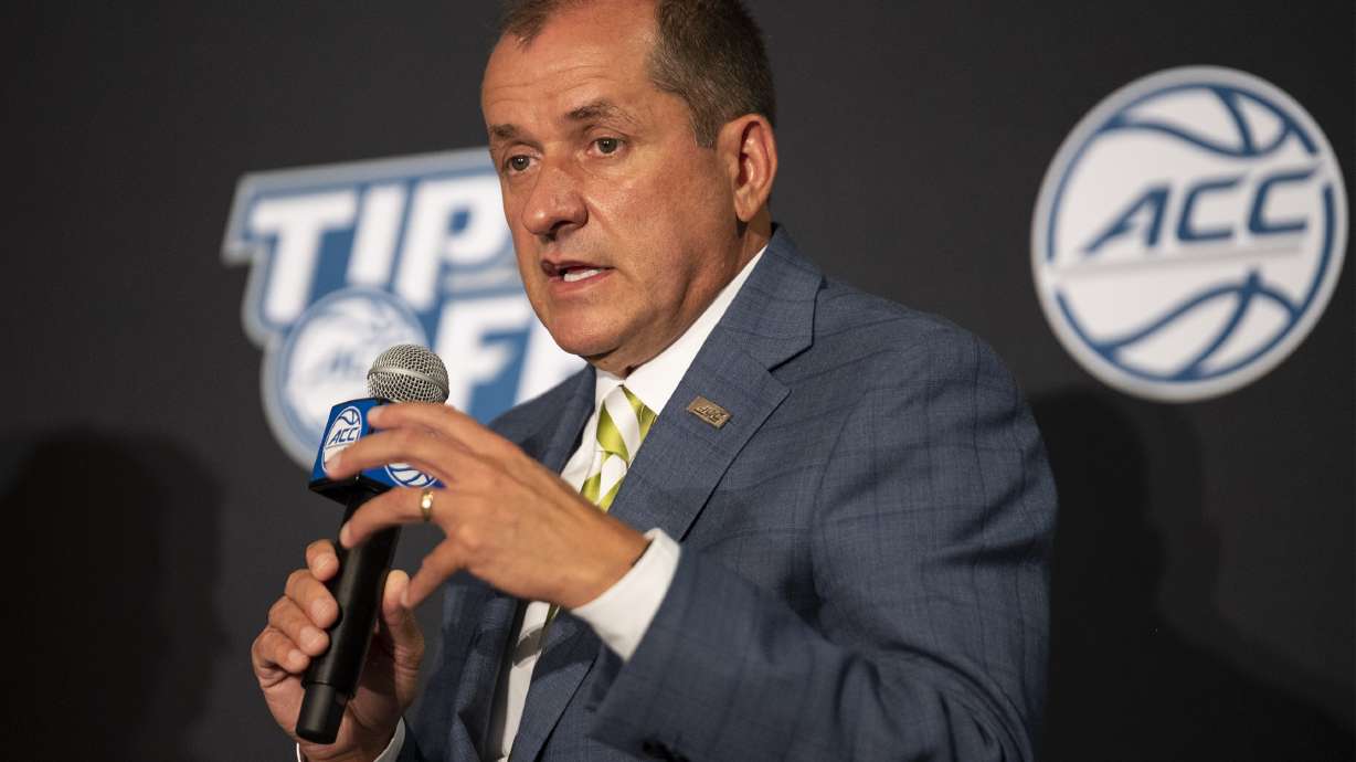 FILE - Atlantic Coast Conference Commissioner Jim Phillips speaks during NCAA college basketball ACC media day, Tuesday, Oct. 12, 2021, in Charlotte, N.C. The ACC is going forward with a plan to change its football scheduling model, with the biggest change being the elimination of divisions. “The future ACC football scheduling model provides significant enhancements for our schools and conference, with the most important being our student-athletes having the opportunity to play every school both home and away over a four-year period,” ACC Commissioner Jim Phillips said.