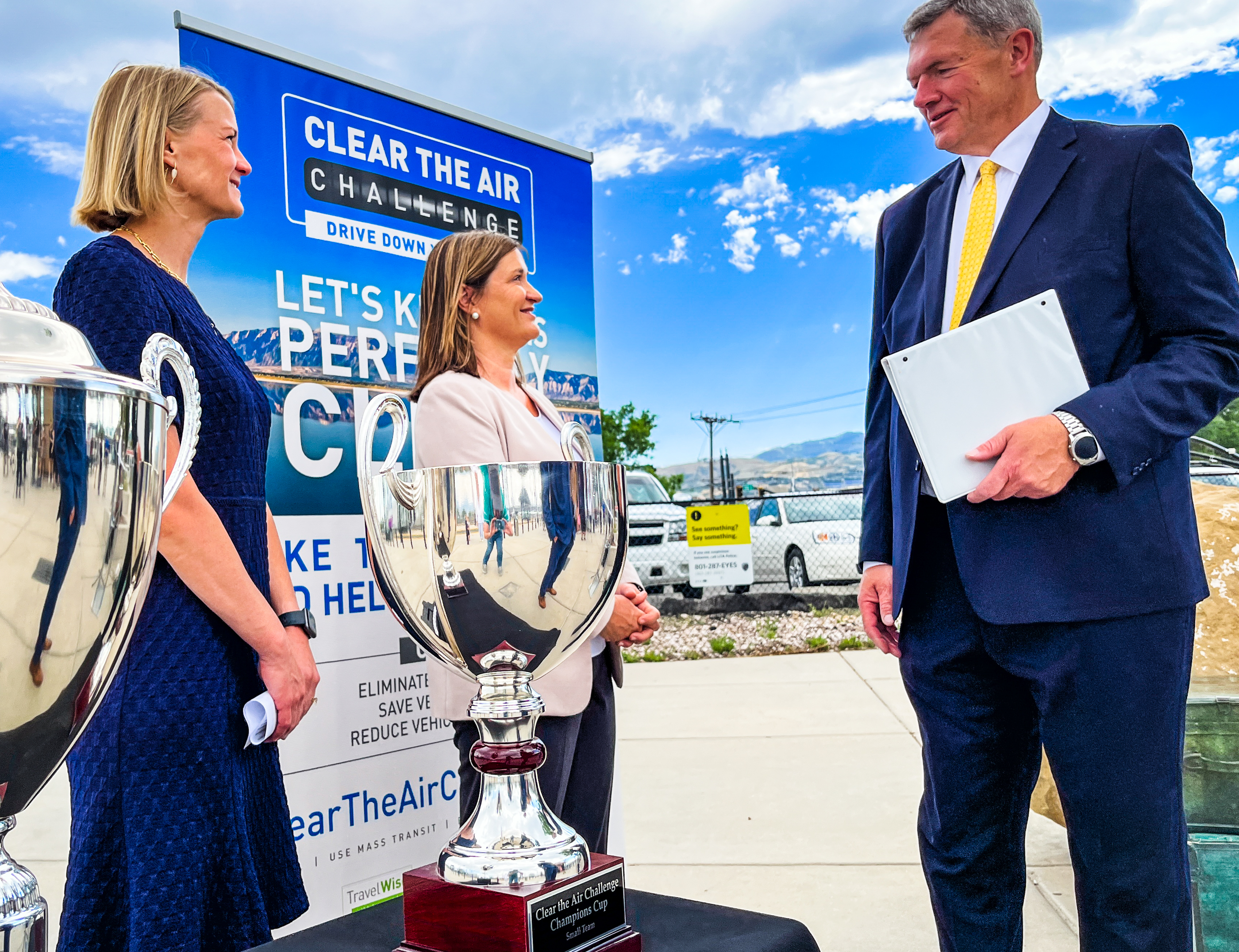 Kim Frost, the executive director of the Utah Clean Air Partnership, left, Salt Lake County Mayor Jenny Wilson, center, and Utah Transit Authority board of trustees Chairman Carlton Christensen chat in front of a pair of trophies up for grabs as a pair of the "Clear The Air Challenge" that begins on Friday.