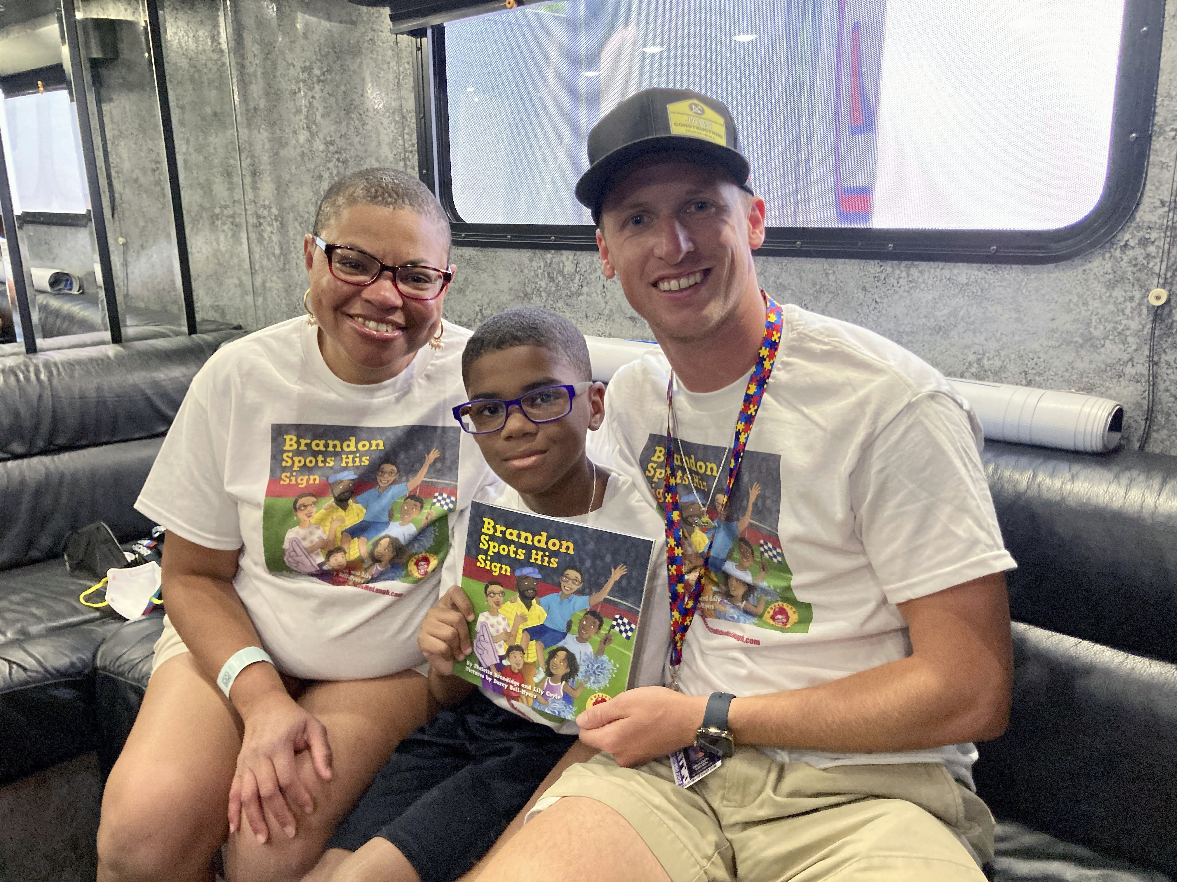 Sheletta Brundidg, left, her son Brandon, center, and NASCAR driver Brandon Brown gather Saturday, July 2, 2022 at Road America in Elkhart Lake, Wis. Sheletta Brundidge wrote a children’s book in her son’s honor after Brandon Brundidge saw “Let’s go, Brandon” signs and assumed they were cheering him on. The cover of Brundidge’s book decorated the hood of Brandon Brown’s car for his Xfinity Series race Saturday at Road America. 