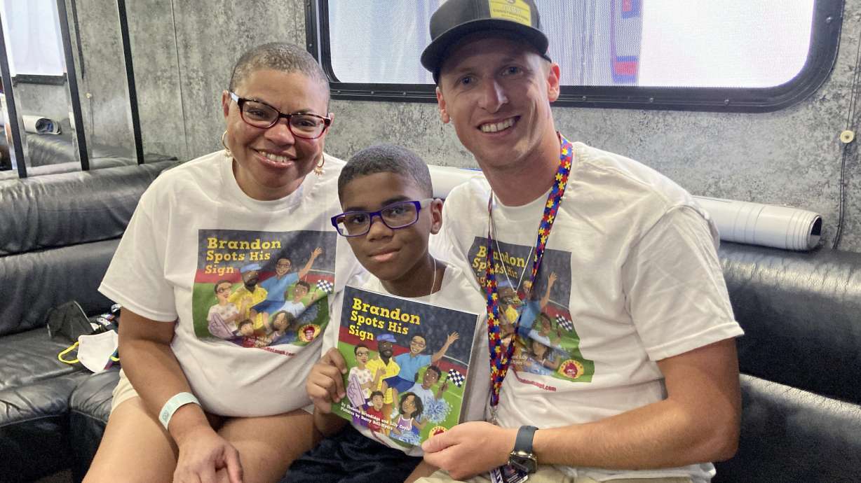 Sheletta Brundidg, left, her son Brandon, center, and NASCAR driver Brandon Brown gather Saturday, July 2, 2022 at Road America in Elkhart Lake, Wis. Sheletta Brundidge wrote a children’s book in her son’s honor after Brandon Brundidge saw “Let’s go, Brandon” signs and assumed they were cheering him on. The cover of Brundidge’s book decorated the hood of Brandon Brown’s car for his Xfinity Series race Saturday at Road America.