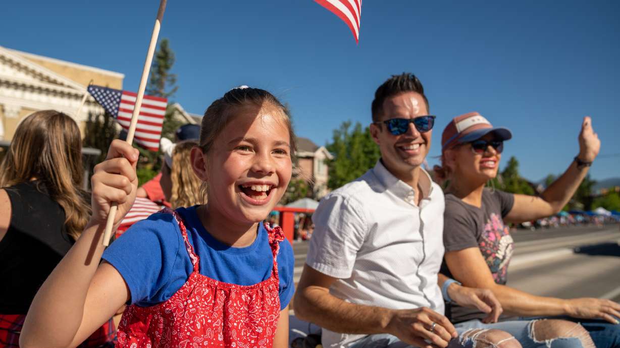 Azalea Osmond, 11, waves a flag as she sits to left of her parents, David and Vallerie, during the America's Freedom Festival Grand Parade in Provo on Monday.