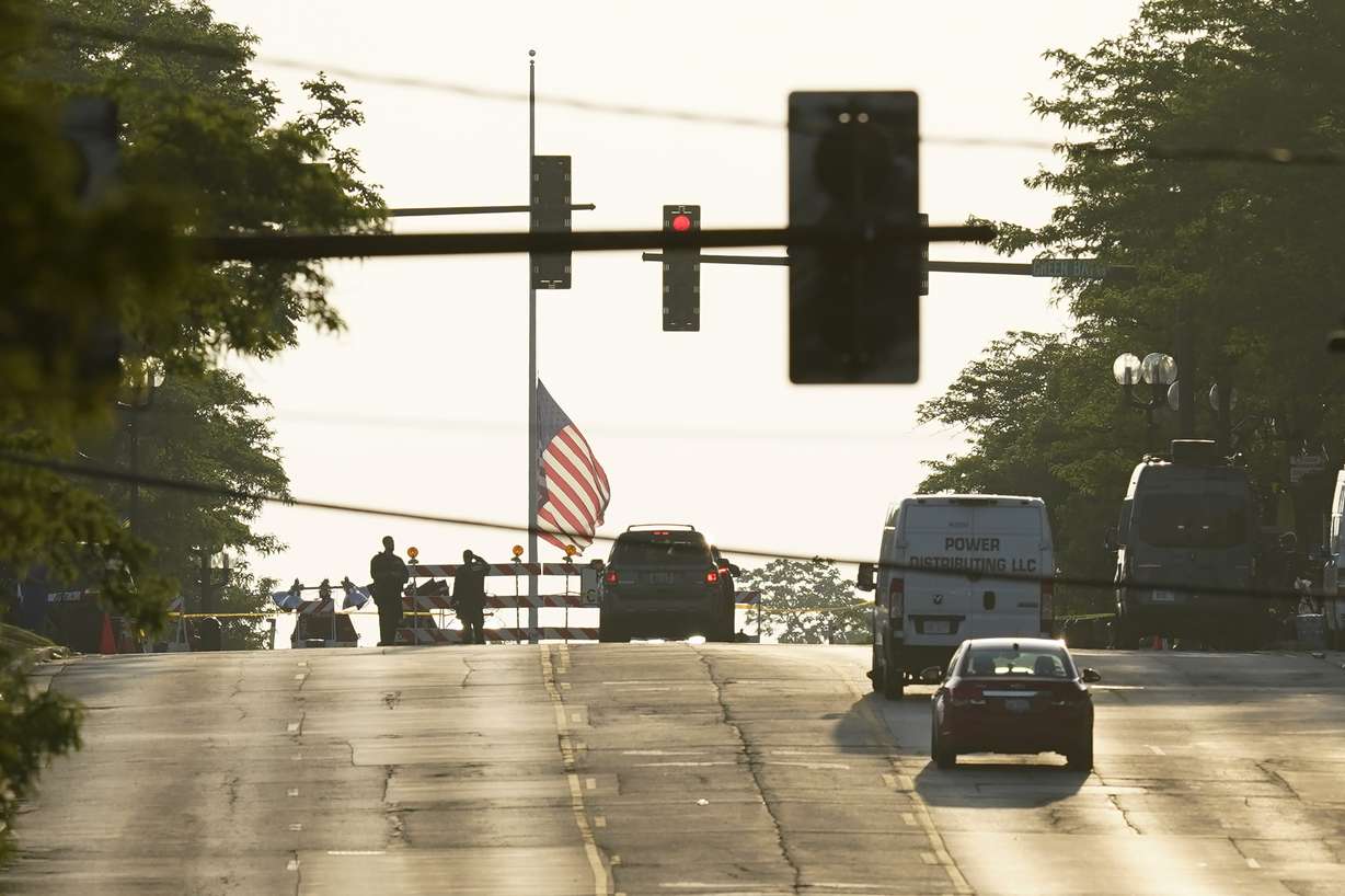 Two police officers stand their post, the day after a deadly mass shooting on the Westside of Highland Park, Ill., Tuesday, as the American flag flies at half-staff on the Eastside.