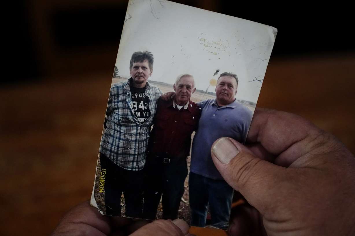 Daniel Guess holds a photograph of himself, right, along with his father, Larry Guess, center, and brother David Guess, left, on June 23, in Athens, Ala.