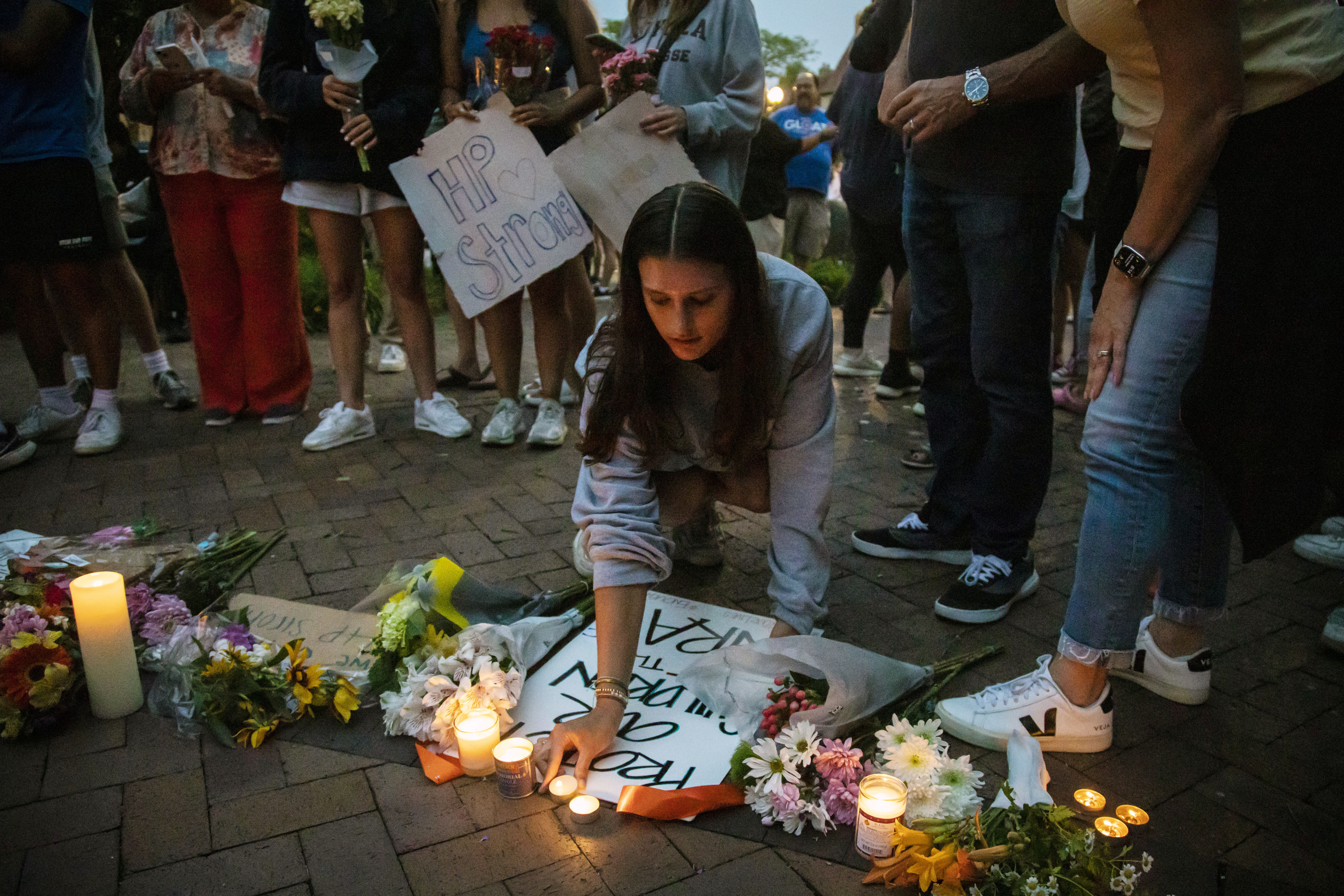 Dozens of mourners gather for a vigil near Central Avenue and St. Johns Avenue in downtown Highland Park, one day after a gunman killed at least seven people and wounded dozens more by firing an AR-15-style rifle from a rooftop onto a crowd attending Highland Park's Fourth of July parade, Tuesday, in Highland Park, Ill.