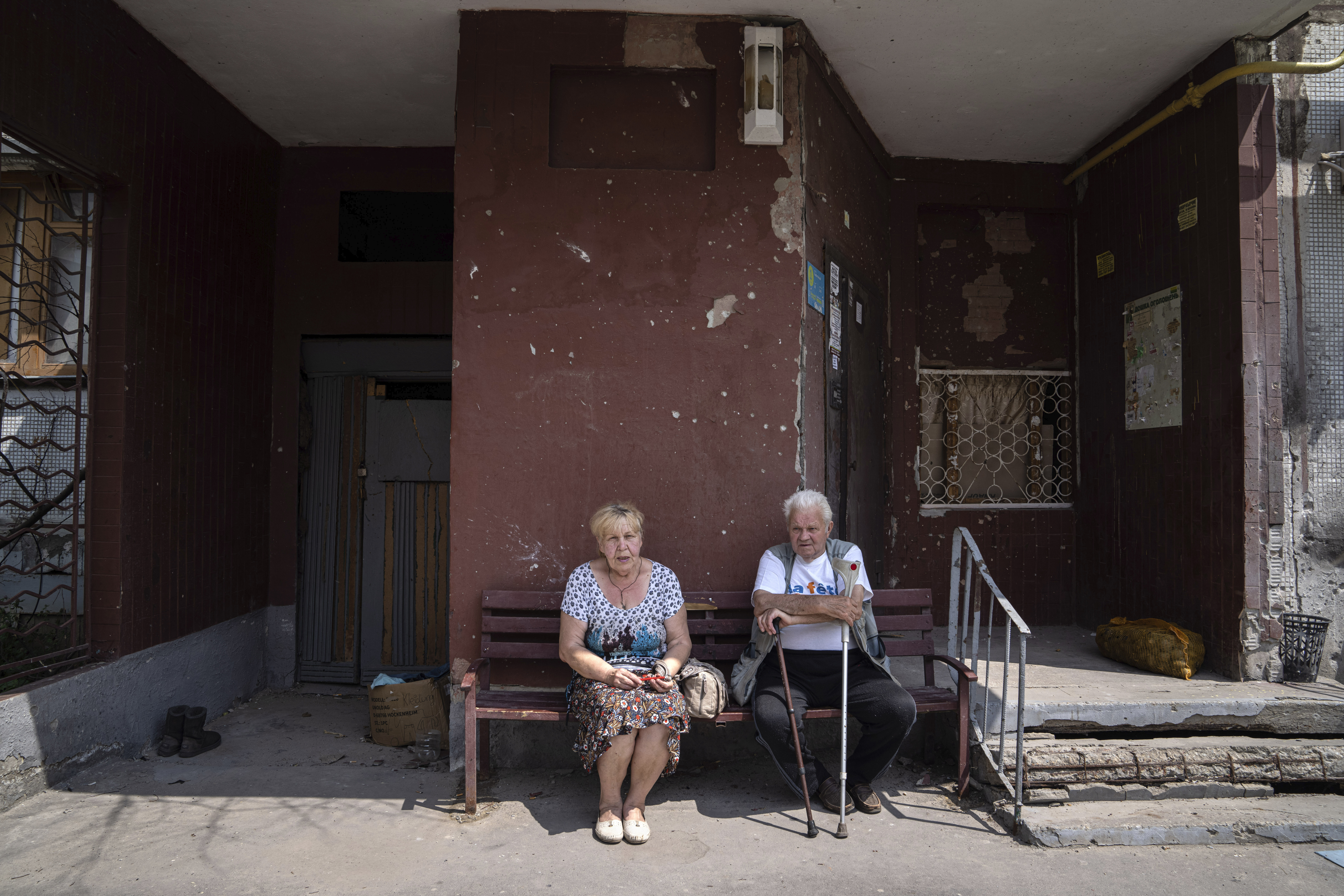 FILE - Pavel Govoryhov, 84, and Tatiana Koneva, 75, residents of Saltivka district, sit on a bench in front of their apartment house in Kharkiv, Ukraine, July 5, 2022. As Russia's invasion of Ukraine grinds into its fifth month, some residents close to the front lines remain in shattered and nearly abandoned neighborhoods. One such place is Kharkiv's neighborhood of Saltivka, once home to about half a million people. Only perhaps dozens live there now, in apartment blocks with no running water and little electricity.