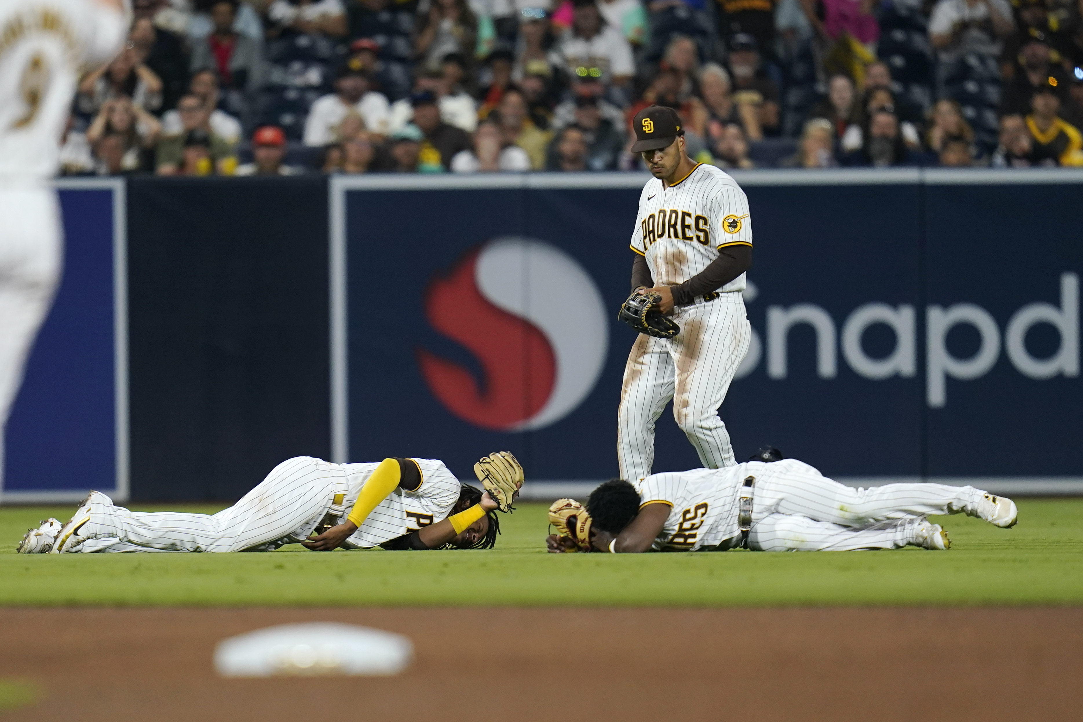 San Diego Padres shortstop C.J. Abrams, left, and left fielder Jurickson Profar, bottom right, react after colliding as center fielder Trent Grisham, center, looks on during the fifth inning of a baseball game against the San Francisco Giants, Thursday, July 7, 2022, in San Diego. Profar and Abrams collided as Abrams made a catch for an out against Giants' Tommy La Stella. 