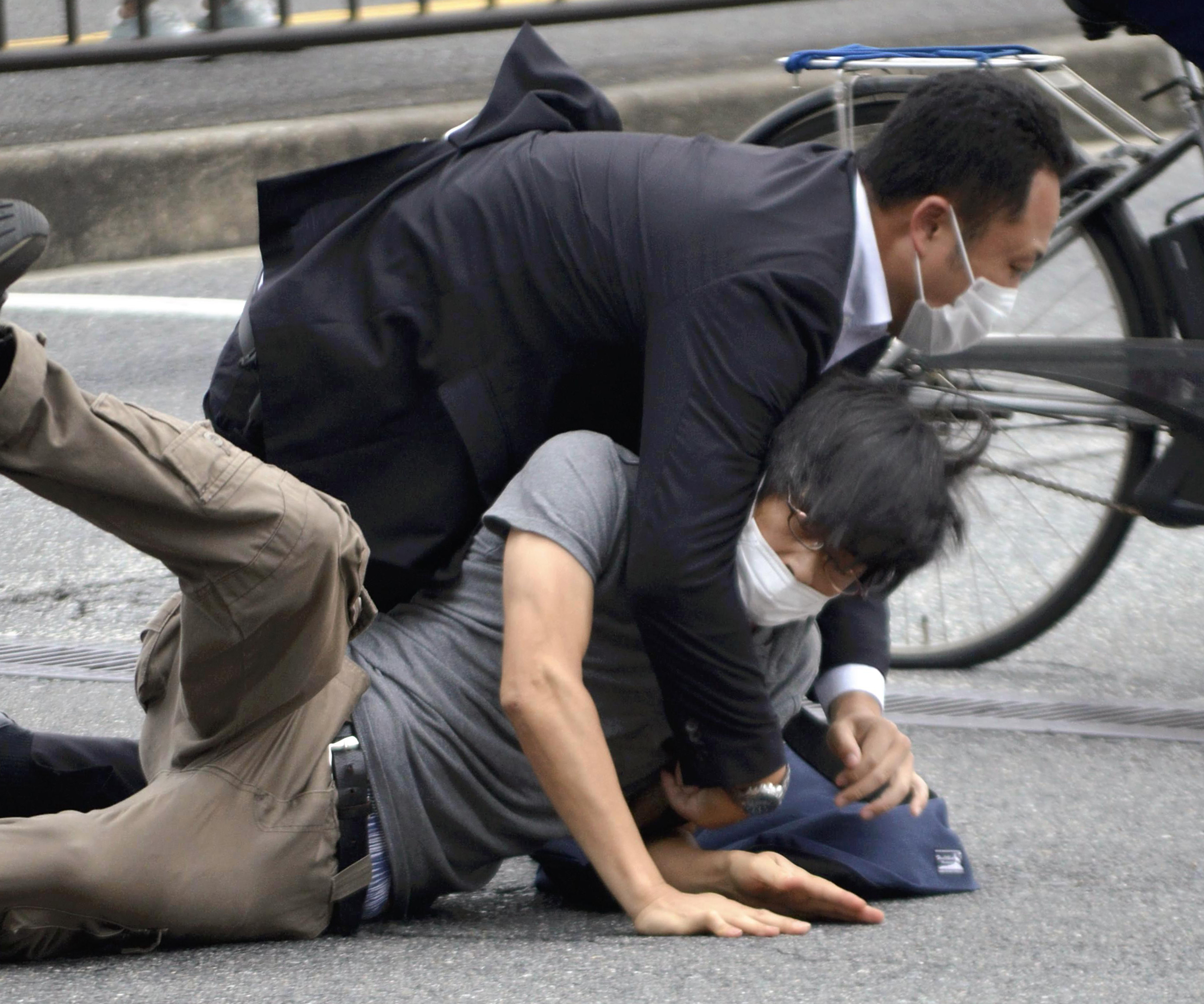 Tetsuya Yamagami, bottom, is detained near the site of gunshots in Nara Prefecture, western Japan, Friday.