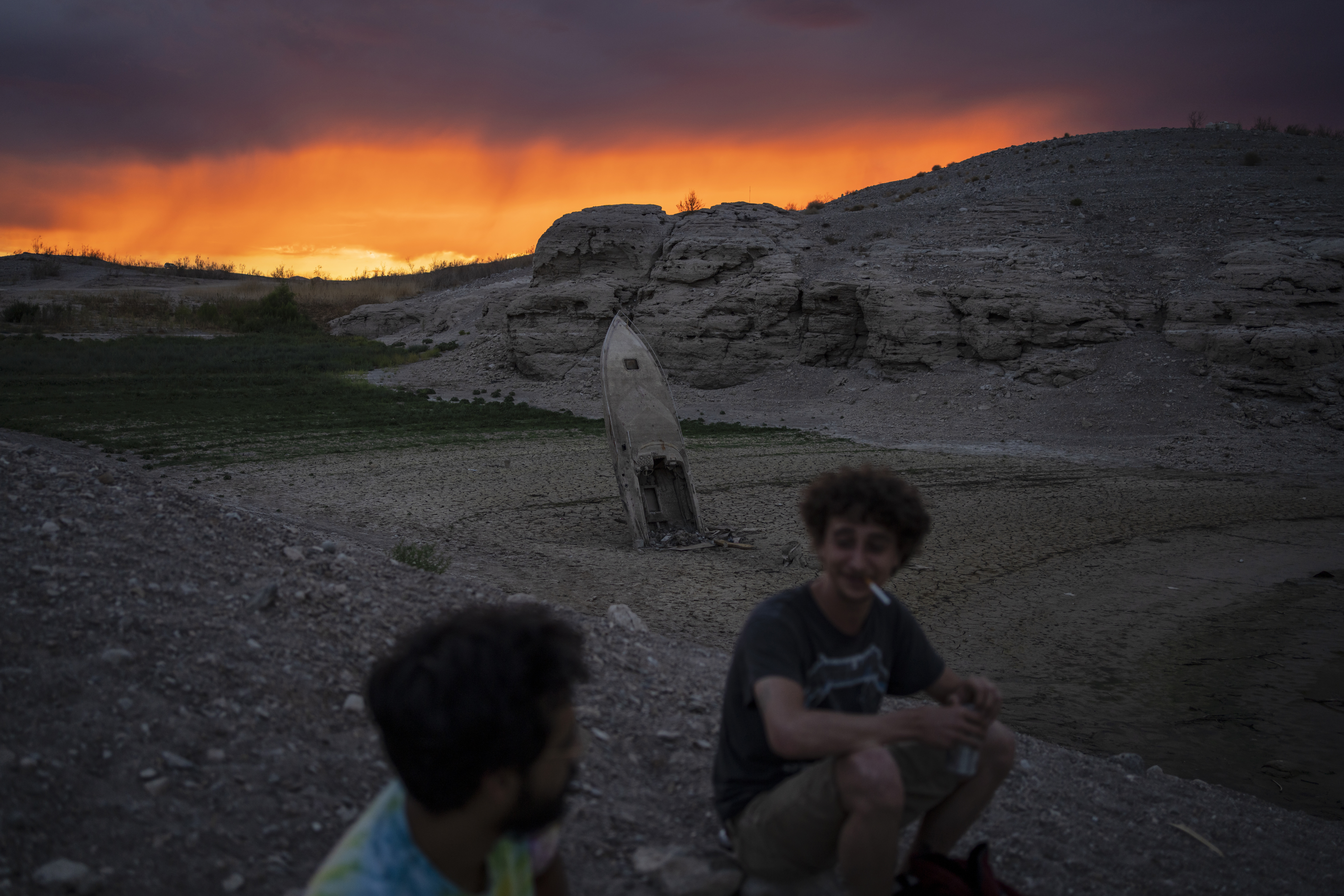 Bobby Rhinebolt, right, smokes a cigarette while sitting beside Victor Perez near a formerly sunken boat implanted upright in mud and now above the water line at the Lake Mead National Recreation Area, June 22, near Boulder City, Nev. As the water level at the lake recedes, sunken boats and other debris are appearing along the shoreline.