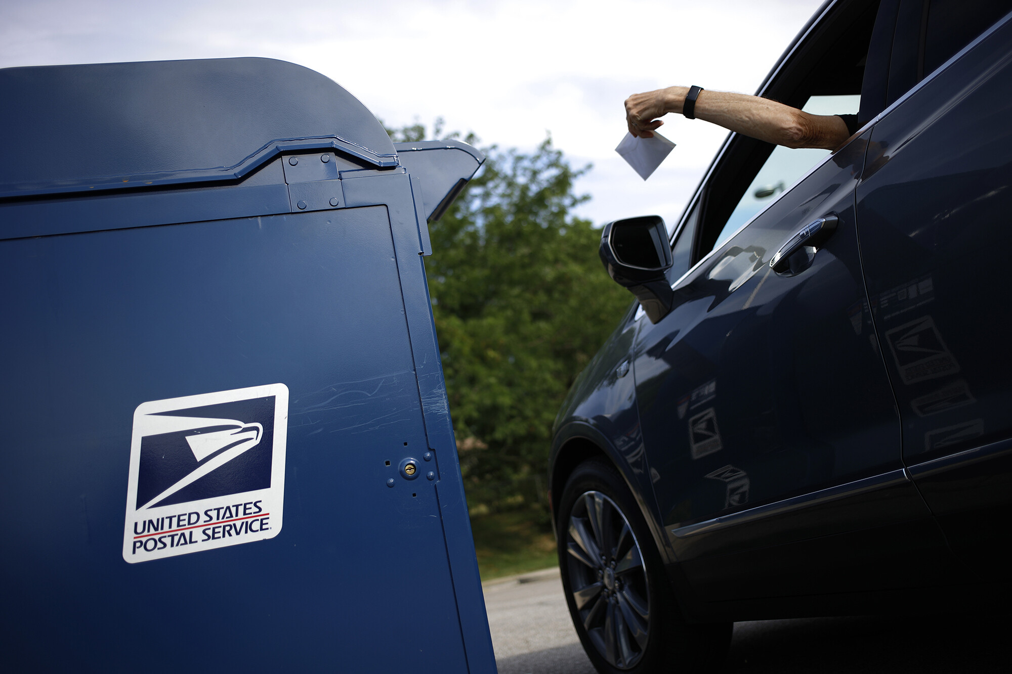 A motorist drops a letter into a United States Postal Service mail drop box in Covington, Kentucky, on July 2. The cost of a US postage stamp just increased by a mere 2 cents.