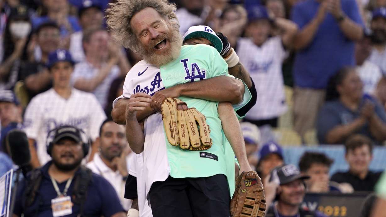 Actor Bryan Cranston is lifted by former Los Angeles Dodgers player Andre Ethier during the MLB All Star Celebrity Softball game, Saturday, July 16, 2022, in Los Angeles.
