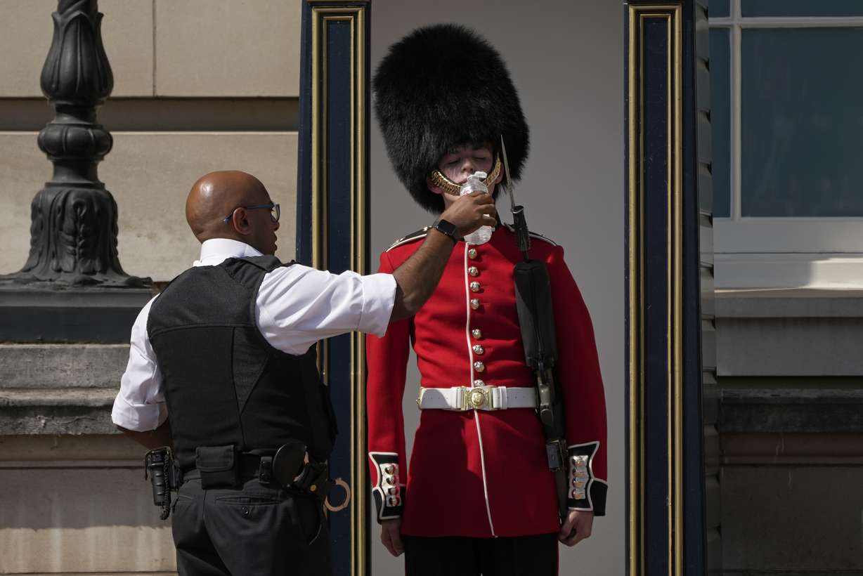 A police officer givers water to a British soldier wearing a traditional bearskin hat, on guard duty outside Buckingham Palace, during hot weather in London, Monday.