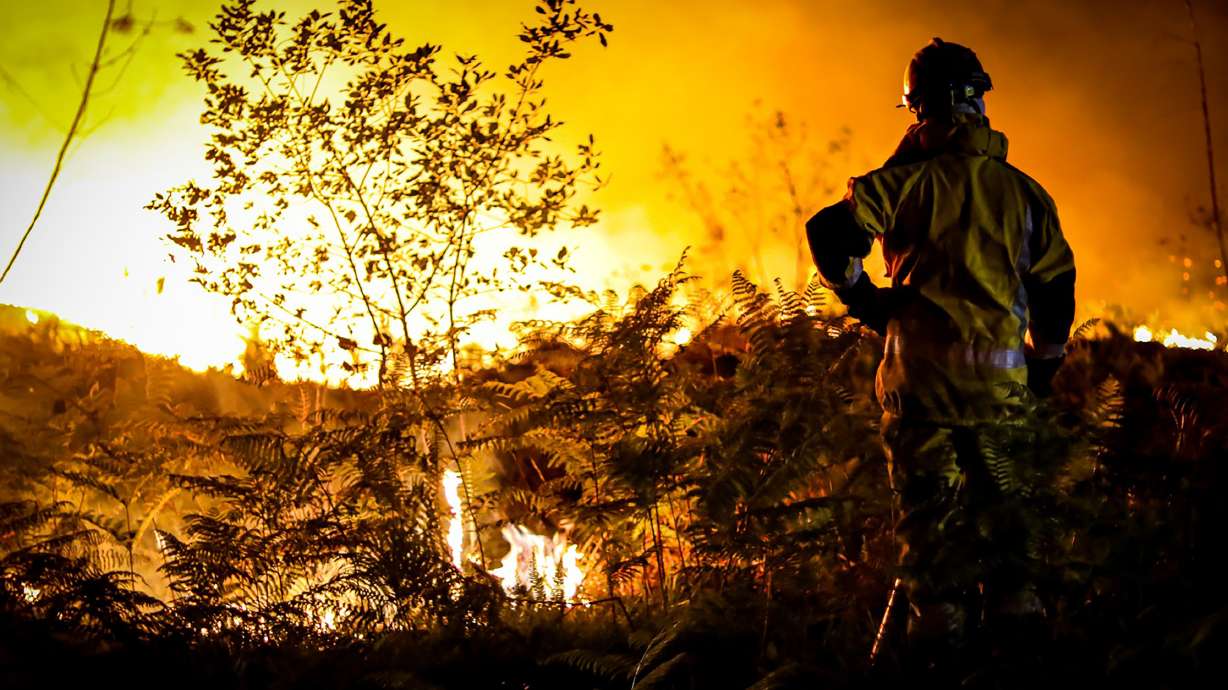 This photo provided by the fire brigade of the Gironde region shows a firefighter standing next to wildfire near Landiras, southwestern France, Monday morning. France scrambled more water-bombing planes and hundreds more firefighters to combat spreading wildfires that were being fed Monday by hot swirling winds from a searing heat wave.