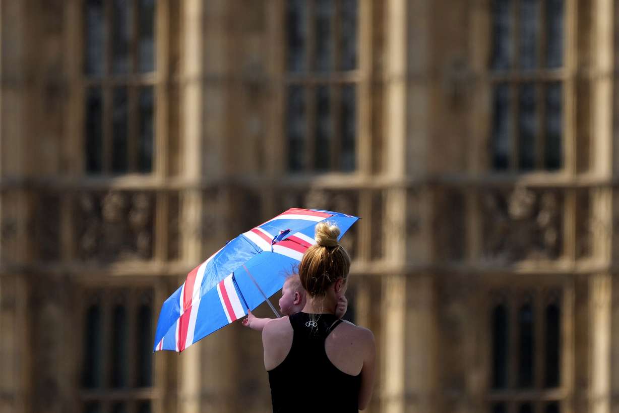 A mother shelters her baby from the sun with an umbrella on Westminster Bridge in London, Tuesday. Britain shattered its record for highest temperature ever registered amid a heat wave that has seized swaths of Europe.