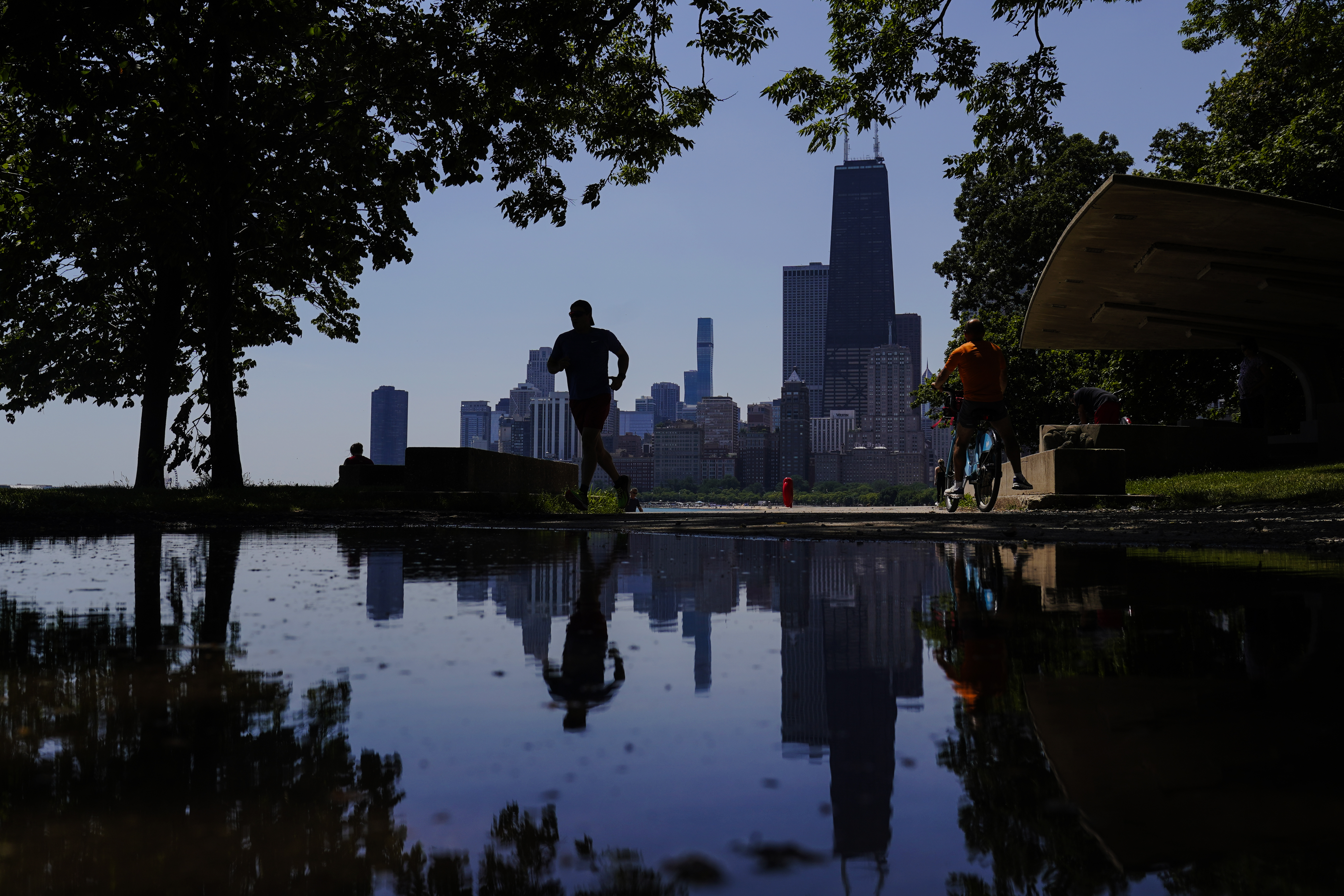 A runner jogs along a path on the shore of Lake Michigan as the downtown skyline is seen in the background, Tuesday, July 19, 2022, in Chicago. 