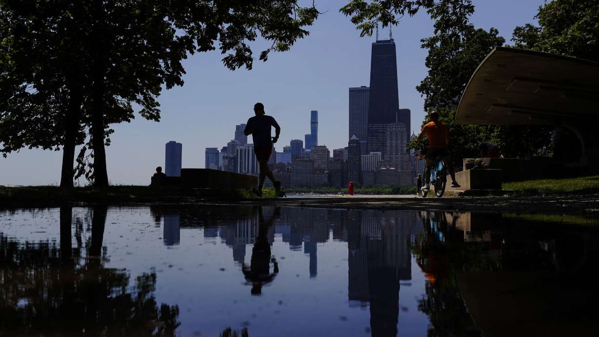 A runner jogs along a path on the shore of Lake Michigan as the downtown skyline is seen in the background, Tuesday, July 19, 2022, in Chicago.