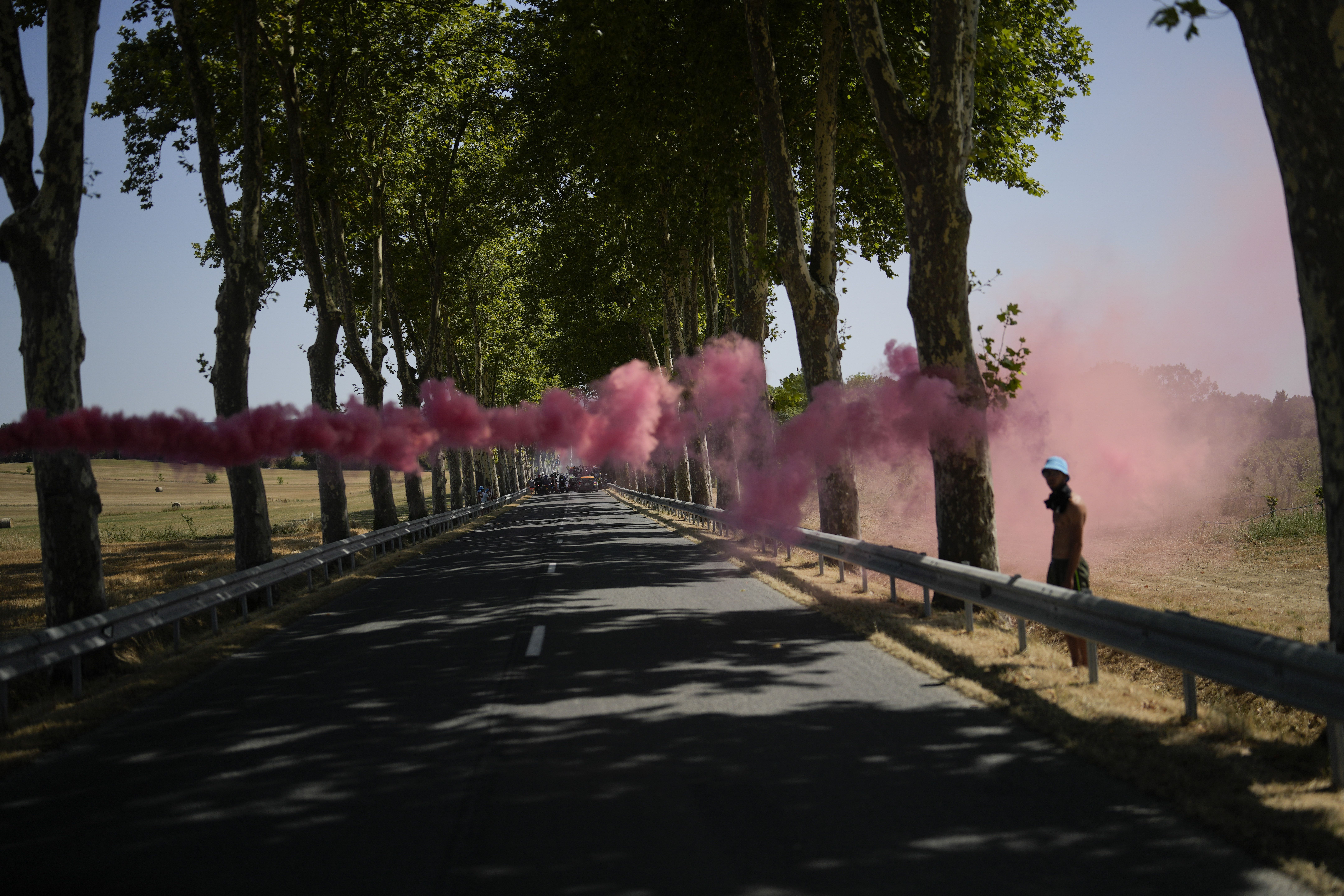 A flare is set off as further down the road climate activists stage a protest during the fifteenth stage of the Tour de France cycling race over 125.5 miles with start in Rodez and finish in Carcassonne, France, Sunday. Environmental activists have disrupted the Tour de France twice since it started in early July, including bringing the three-week bicycle race to a halt on one stage last week.