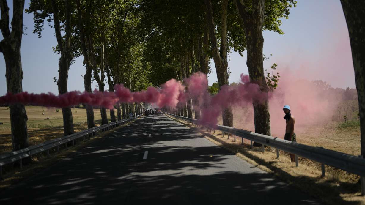 A flare is set off as further down the road climate activists stage a protest during the fifteenth stage of the Tour de France cycling race over 125.5 miles with start in Rodez and finish in Carcassonne, France, Sunday. Environmental activists have disrupted the Tour de France twice since it started in early July, including bringing the three-week bicycle race to a halt on one stage last week.