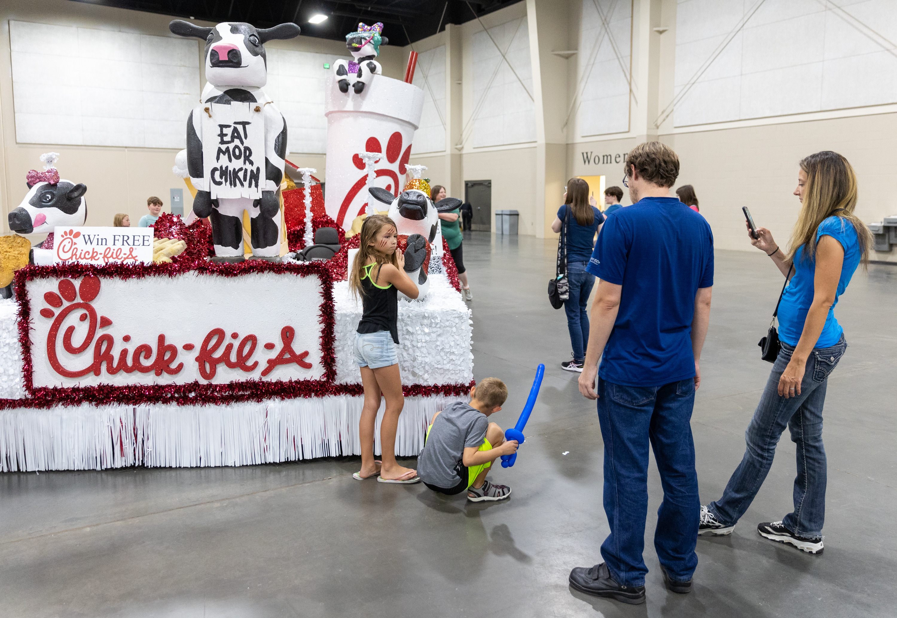 Mikaela Brun, 10, checks out the Chick-Fil-A float while her brother, Liam Brun, 8, squats next to it and the mother, Natalie Brun snaps a photo at the Float Preview Party inside of the Mountain America Expo Center in Sandy on Monday.