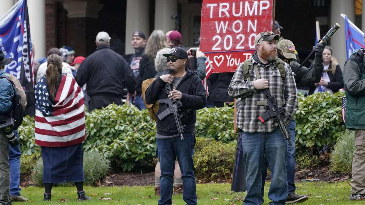 Two men stand armed with guns on Jan. 6, 2021, in front of the Governor's Mansion in Olympia, Wash., during a protest supporting then-President Donald Trump. The key to dispelling conspiracy theories and misinformation about how elections are run is to confront the lies head on, election leaders from across the country who are meeting under heightened security in Wisconsin were told Wednesday.