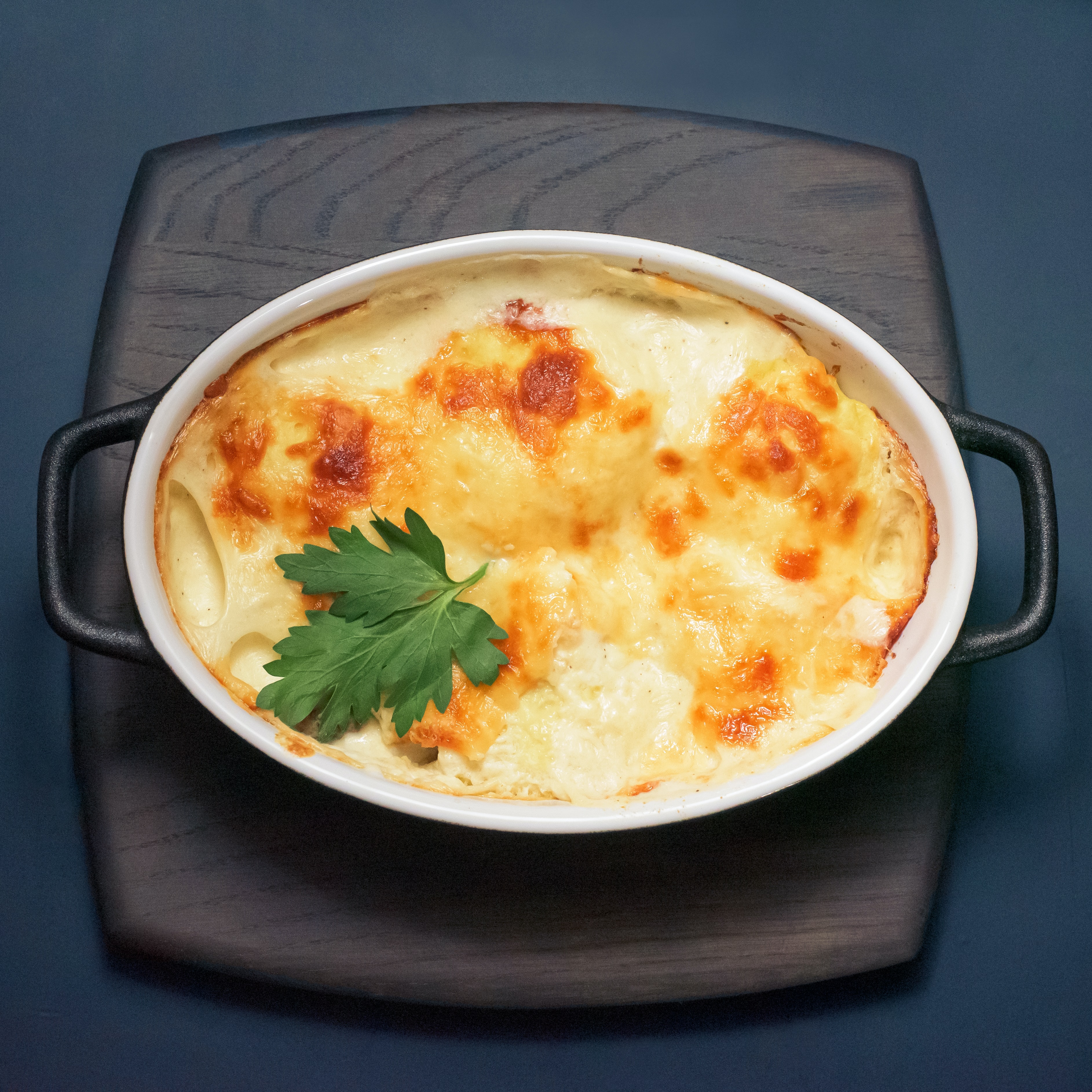 A photograph of a cheesy potato casserole in a white baking dish.