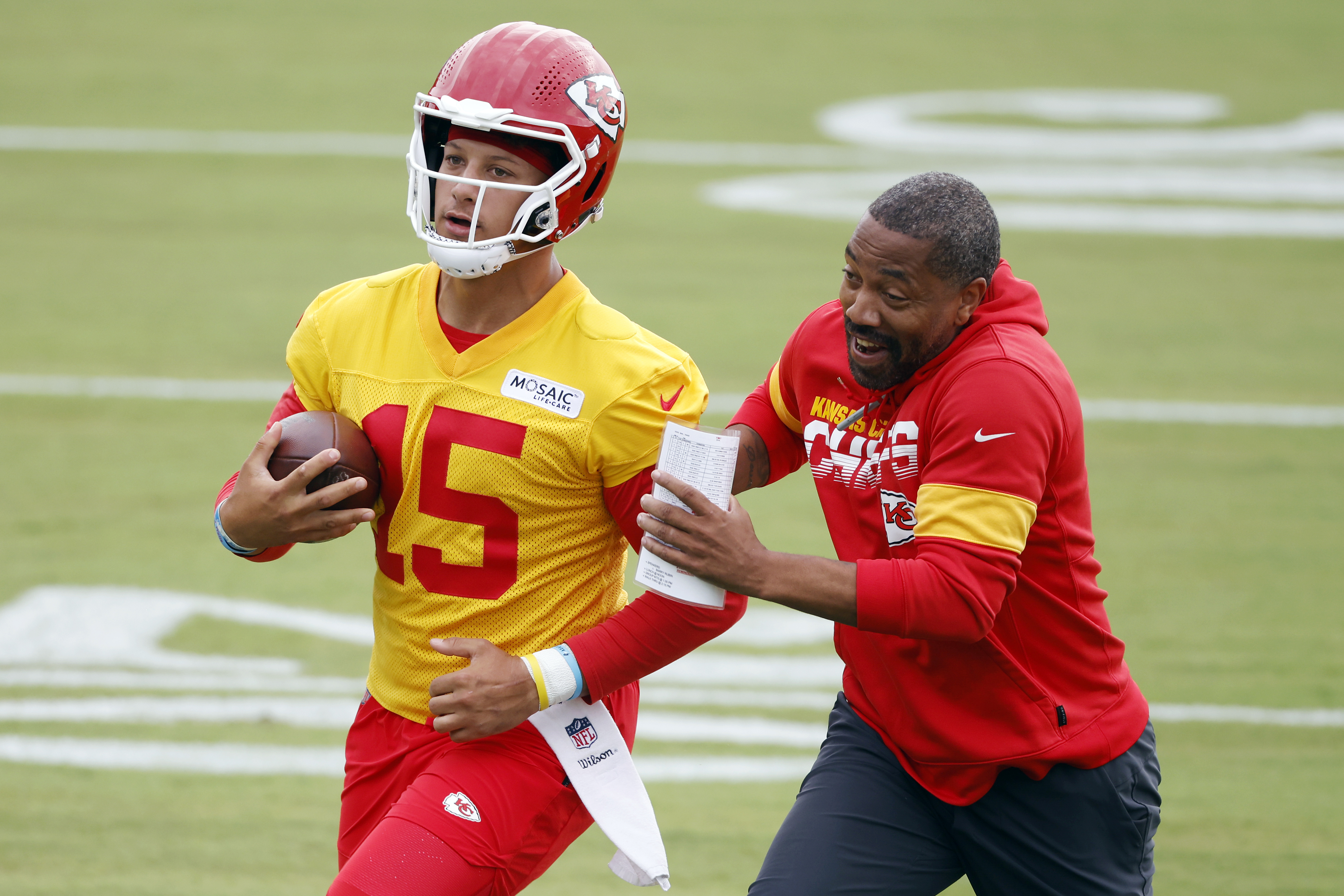 Kansas City Chiefs quarterback Patrick Mahomes (15) completes a running play as running backs coach Greg Lewis pursues during an NFL football training camp at Missouri Western State University in St. Joseph, Mo., Sunday, July 24, 2022. 