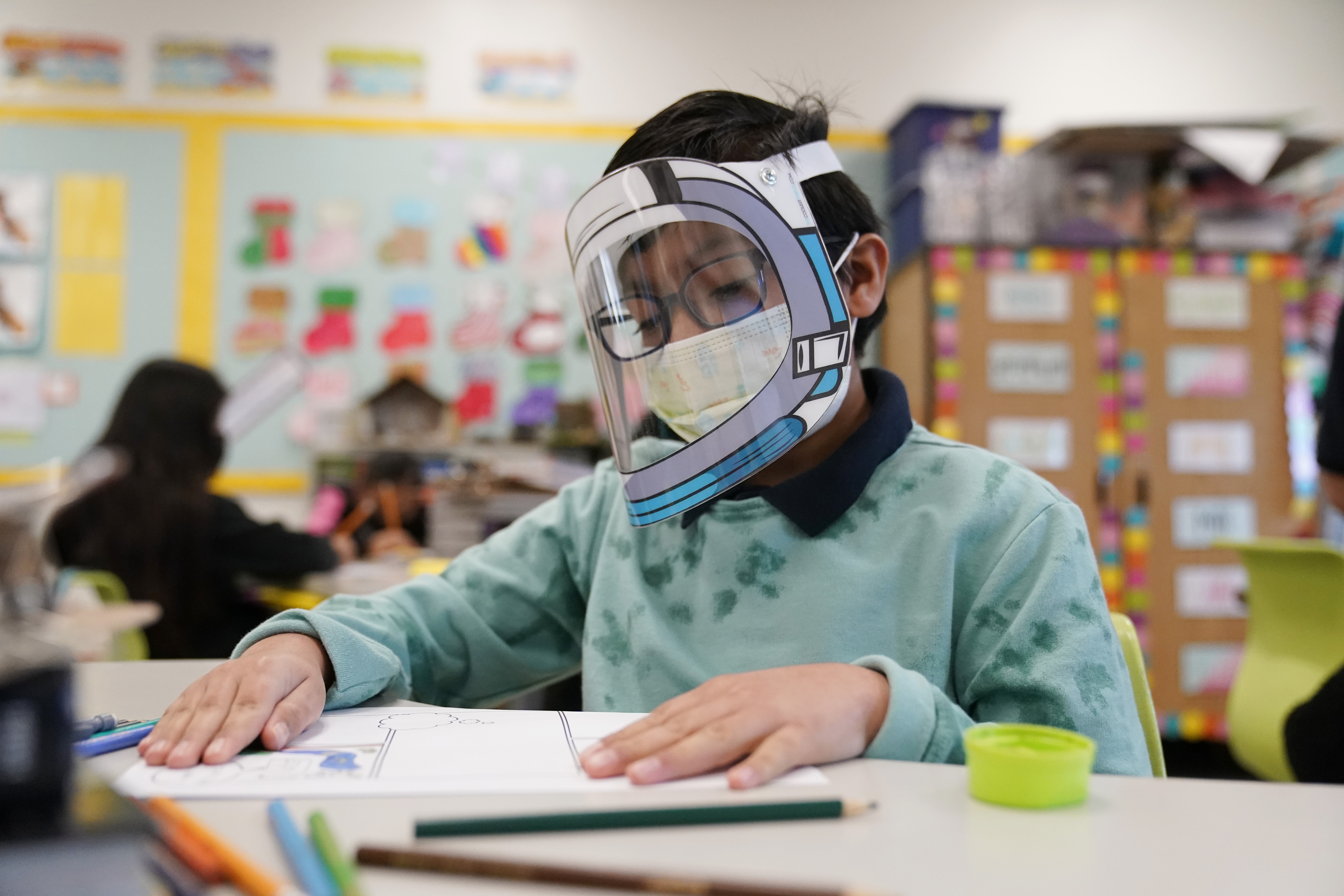 A student wears a mask and face shield in a 4th grade class amid the COVID-19 pandemic at Washington Elementary School on Jan. 12, 2022, in Lynwood, Calif. As a new school year approaches, COVID-19 infections are again on the rise, fueled by highly transmissible variants, filling families with dread.