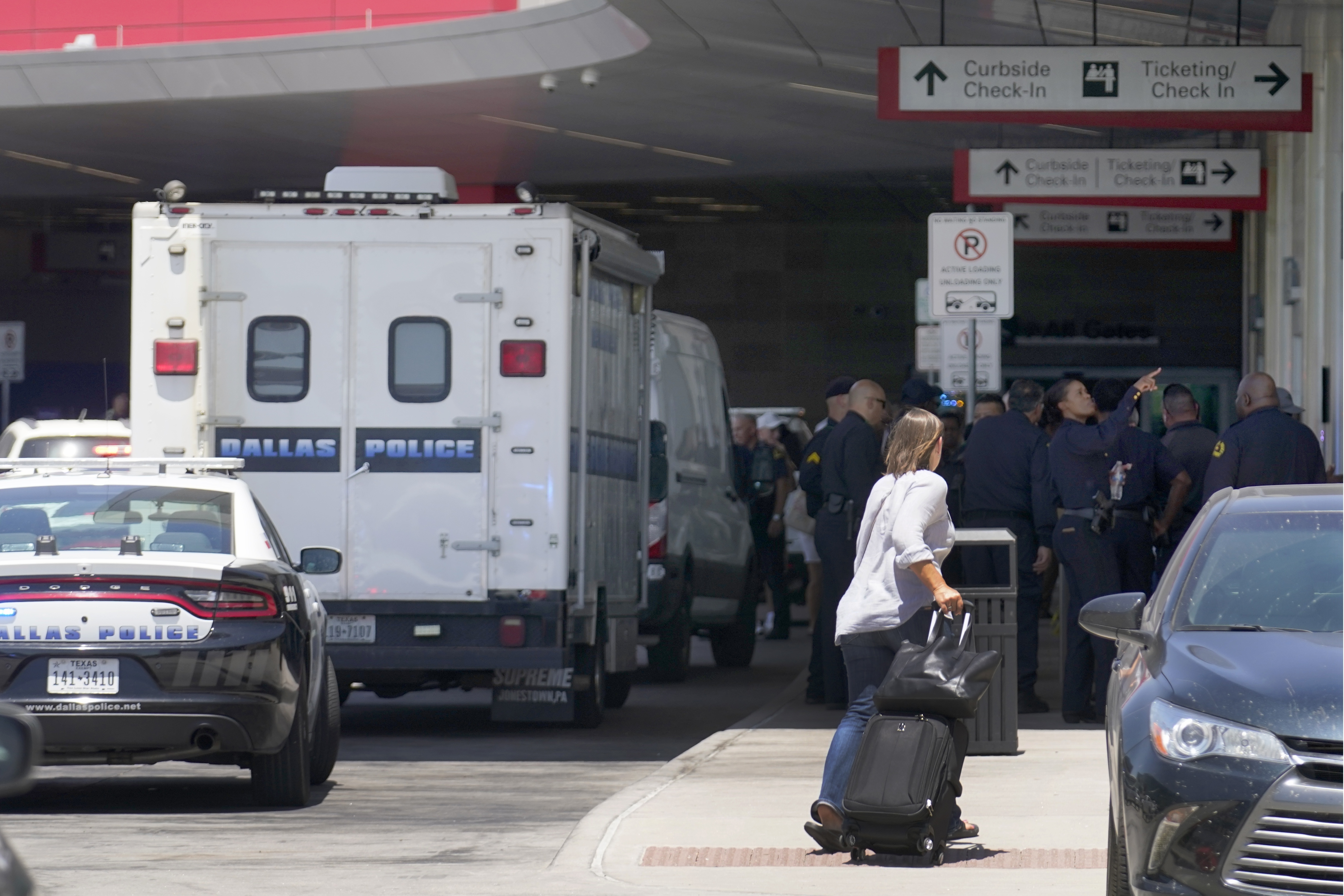 A traveler makes her way past emergency responders standing outside the ticketing and check-in area at Dallas Love Field in Dallas, Monday. A 37-year-old woman fired several gunshots, apparently at the ceiling, inside the airport on Monday before an officer shot and wounded her, authorities said. 