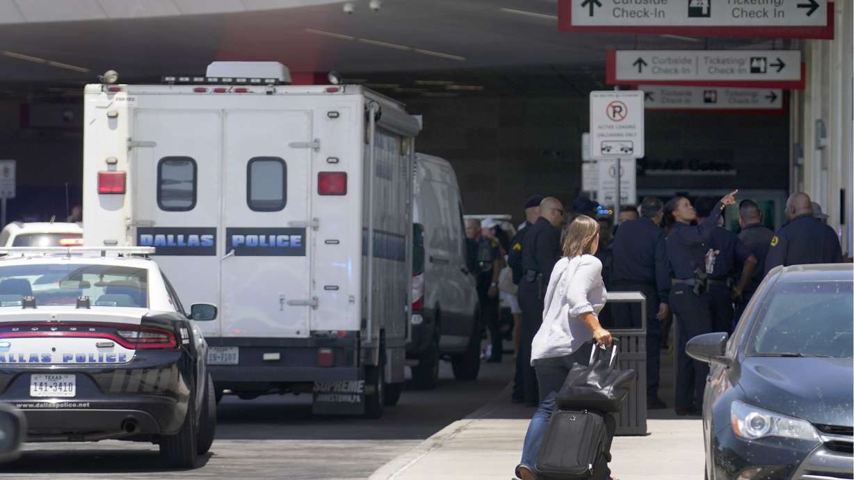 A traveler makes her way past emergency responders standing outside the ticketing and check-in area at Dallas Love Field in Dallas, Monday. A 37-year-old woman fired several gunshots, apparently at the ceiling, inside the airport on Monday before an officer shot and wounded her, authorities said.