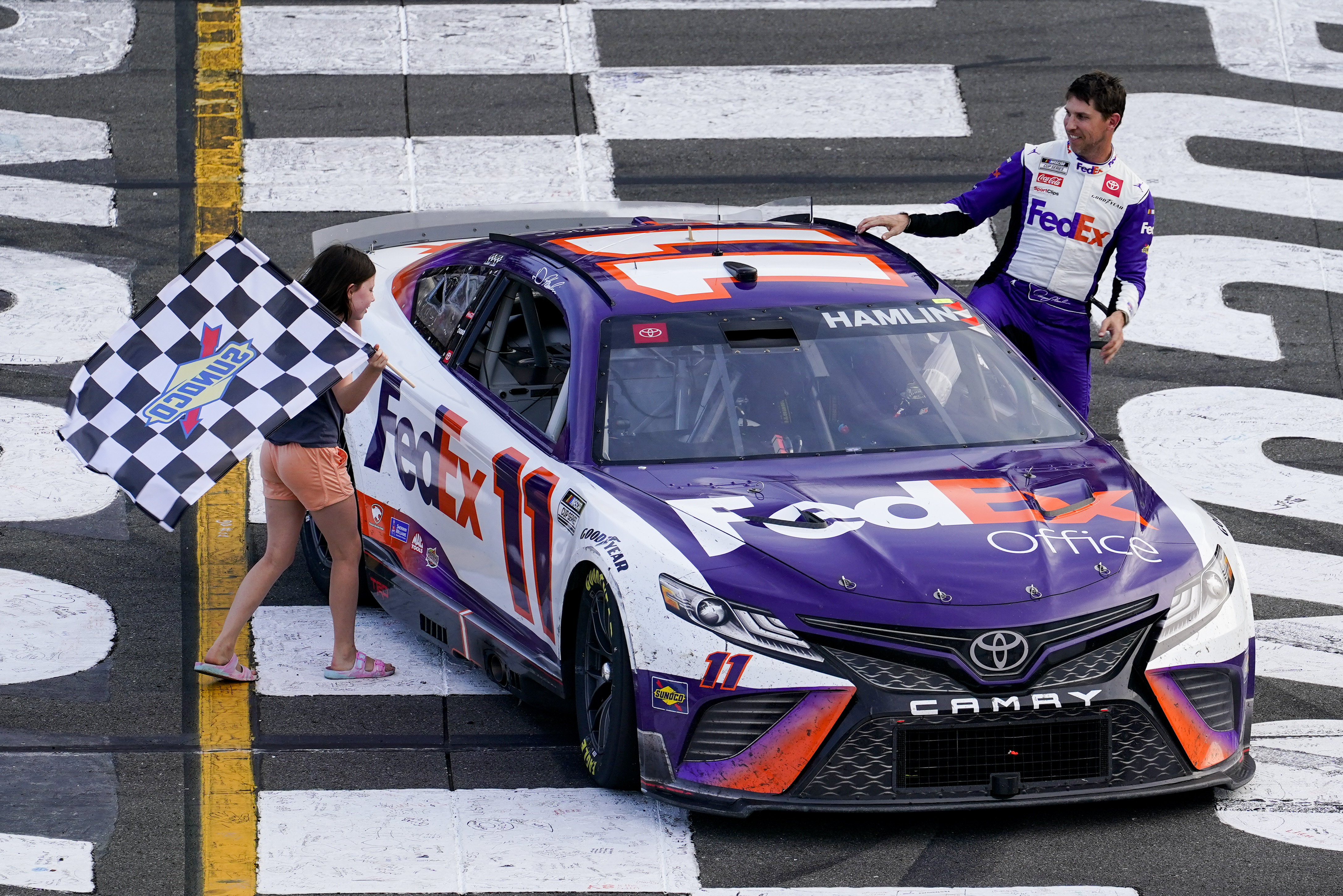 ADDS THAT HAMLIN WAS LATER DISQUALIFIED - Taylor James Hamlin, left, carries the checkered flag with her dad, Denny Hamlin, after he won a NASCAR Cup Series auto race at Pocono Raceway, Sunday, July 24, 2022, in Long Pond, Pa. NASCAR stripped Hamlin of his win when his No. 11 Toyota failed inspection and was disqualified, awarding Chase Elliott the Cup Series victory. 