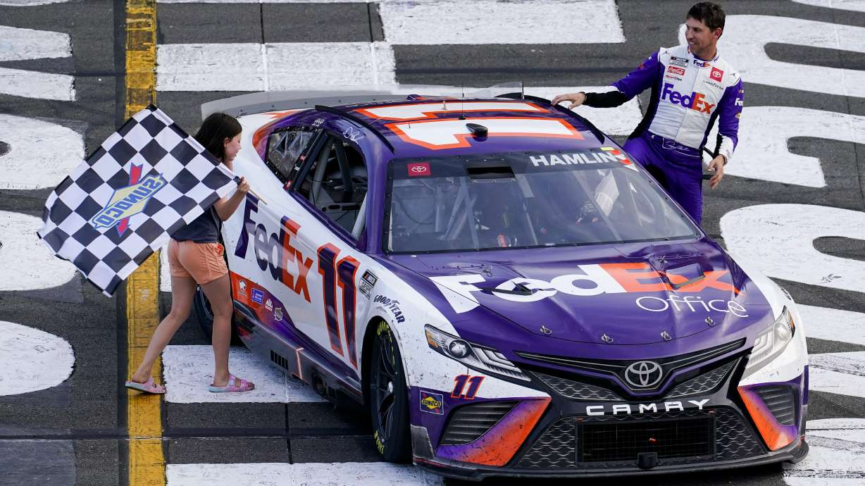 ADDS THAT HAMLIN WAS LATER DISQUALIFIED - Taylor James Hamlin, left, carries the checkered flag with her dad, Denny Hamlin, after he won a NASCAR Cup Series auto race at Pocono Raceway, Sunday, July 24, 2022, in Long Pond, Pa. NASCAR stripped Hamlin of his win when his No. 11 Toyota failed inspection and was disqualified, awarding Chase Elliott the Cup Series victory.