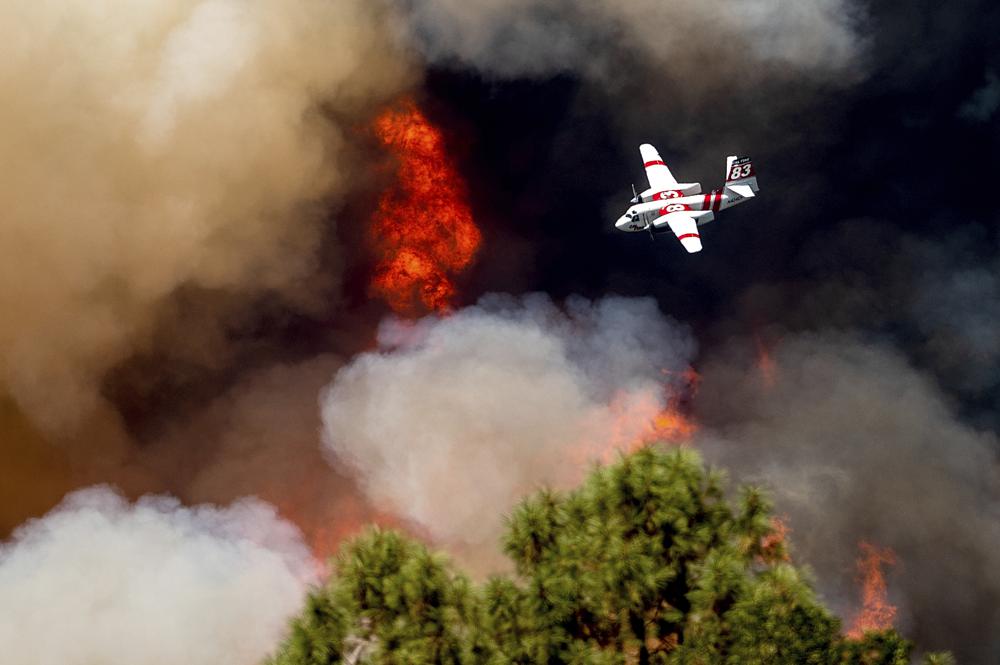 An air tanker flies past flames while battling the Oak Fire in Mariposa County, Calif., Sunday. Wildfires, floods and soaring temperatures have made climate change real to many Americans. Yet a sizeable number continue to dismiss the scientific consensus that human activity is to blame.